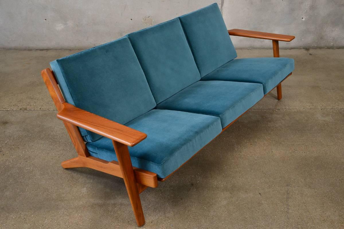 A fantastic Hans Wegner GE-290 sofa designed in 1953 and produced by GETAMA in Denmark. This example is the less common teak version. It has been completely restored. The original sprung cushions have been reupholstered in a beautiful peacock blue