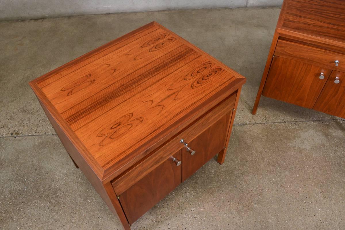 A pair of walnut and rosewood nightstands designed by Paul McCobb as part of the Delineator line for Lane. They offer ample storage with a drawer and large compartment. They look like they may have been previously restored, they do have some