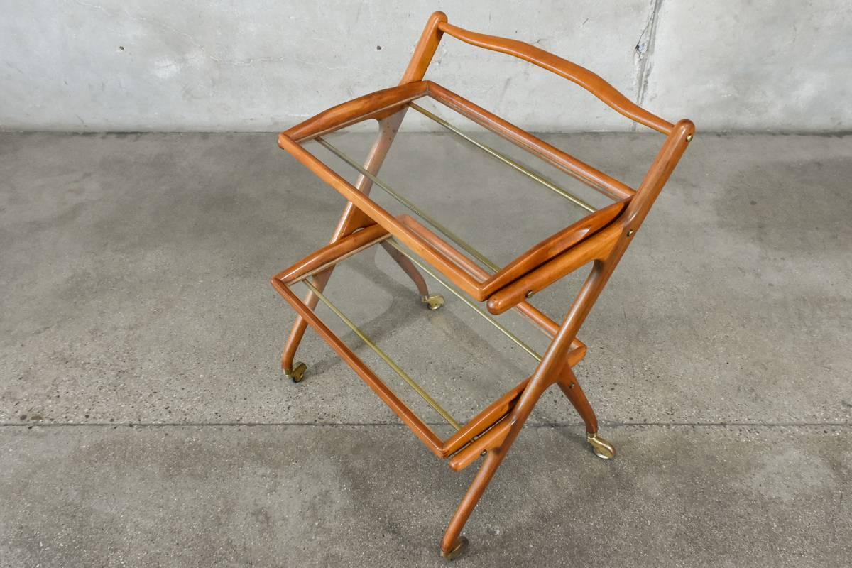 A fantastic sculptural Italian bar cart in the manner of Cesare Lacca. The beautifully shaped wood frame is connected with brass rods that support the removable trays. The original finish shows some cracking that is most notable on the handle as
