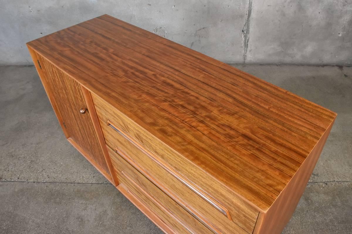 A very nice compact credenza designed by Milo Baughman as part of the Drexel Perspective line in 1952. Utilizing beautiful Mindoro wood throughout the color and grain on this piece is quite stunning. This piece appears to have been refinished, and