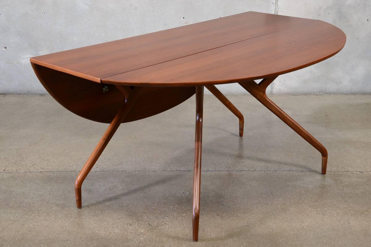 Stunning drop leaf walnut dining table designed by Ed Frank for Glenn of California in the 1950s. This versatile piece makes for a beautiful console with the leaves down, and generously sized dining table with both leaves up. The unique leaves have