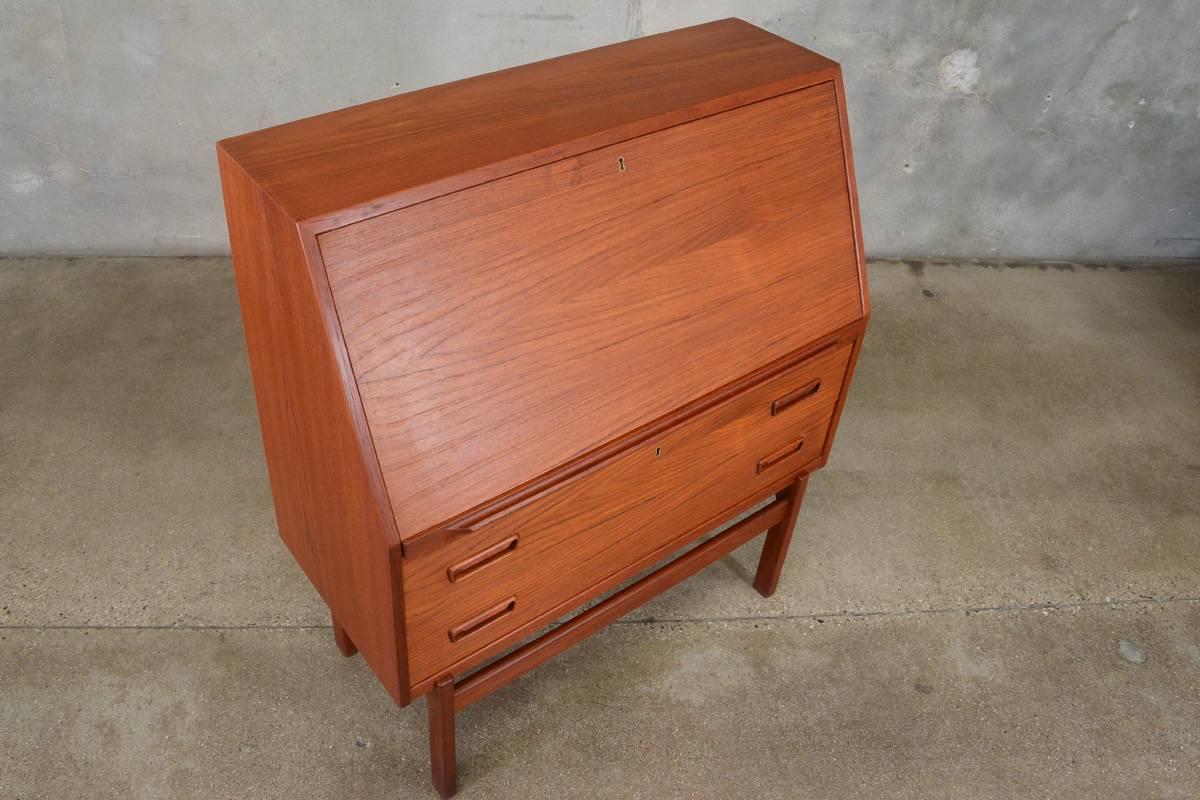 A simple and classic drop front Danish secretary desk. Two large drawers on the lower portion offer ample storage. When open the upper portion offers a large desk area, with some unique slanted drawers and cubbies of varying sizes. This piece is in