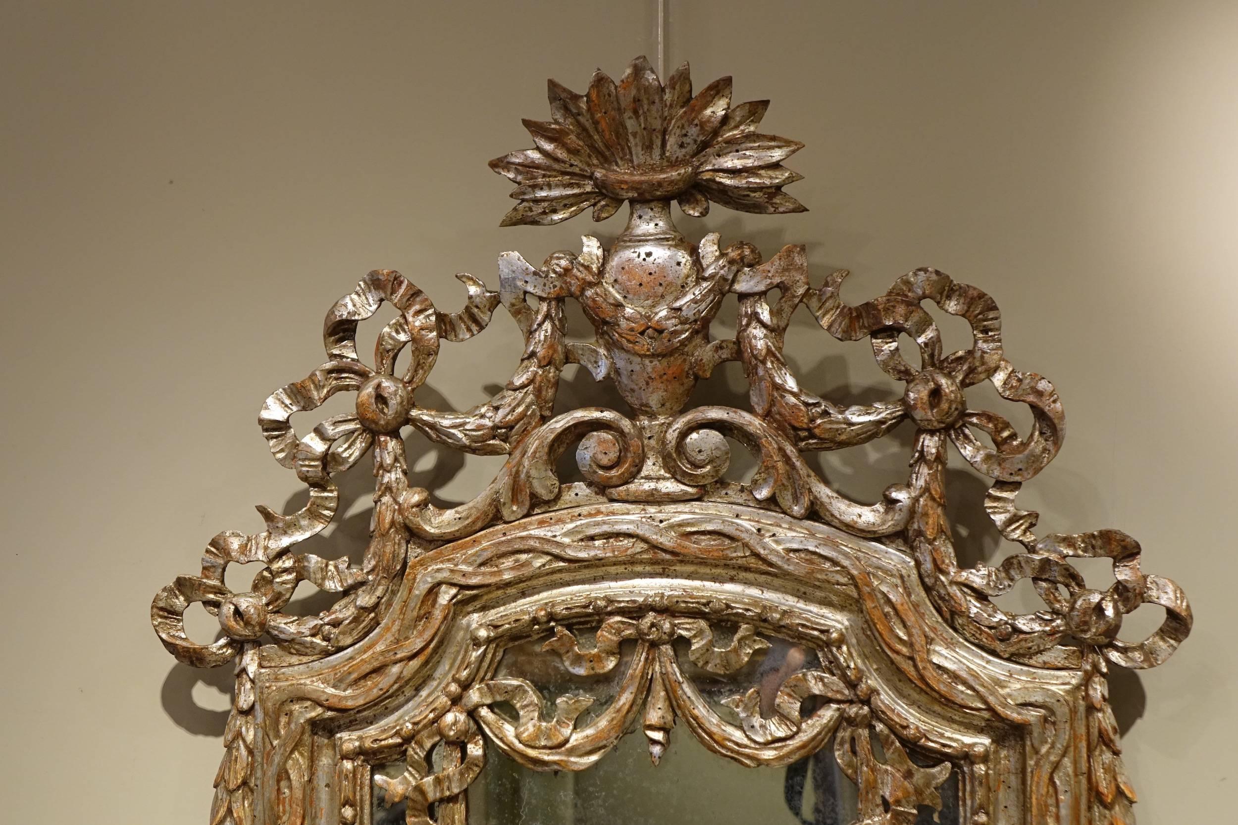 Louis XVI Mirror in carved wood and silver giltwood.
Richly decorated with garlands of flowers and ribbons
Pretty patina and wear due to the time. Overall original silver gilt.
Original mercury coated glass

Provence (or Italy), 18th century.