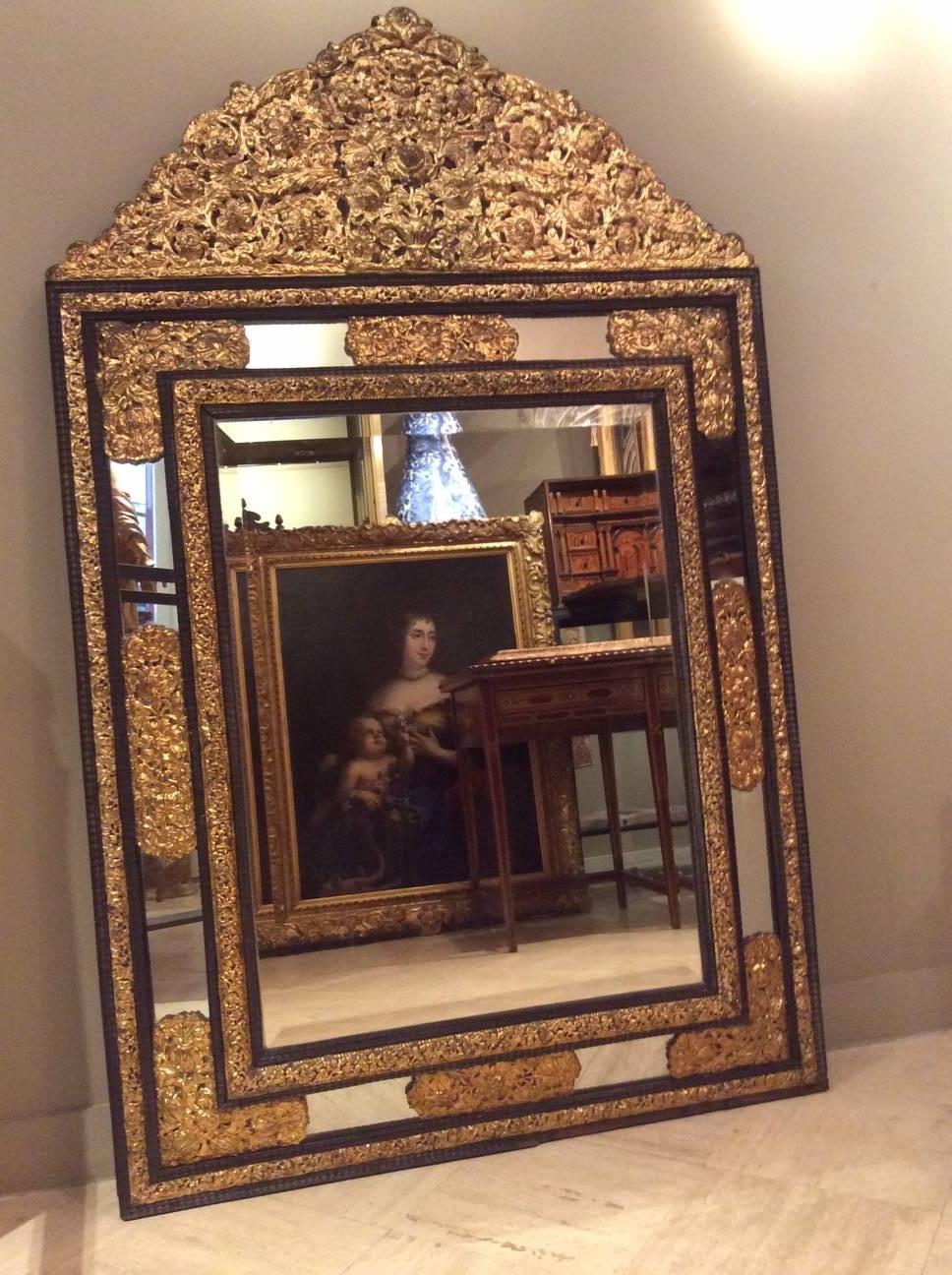 19th century large mirror in the style of Louis XIII in wood and embossed gilded brass, richly decorated with flowers and foliage. 
Beautiful frieze guilloched in ebony wood.
Original mercury, beveled central glass mirror.
France, circa 1850.