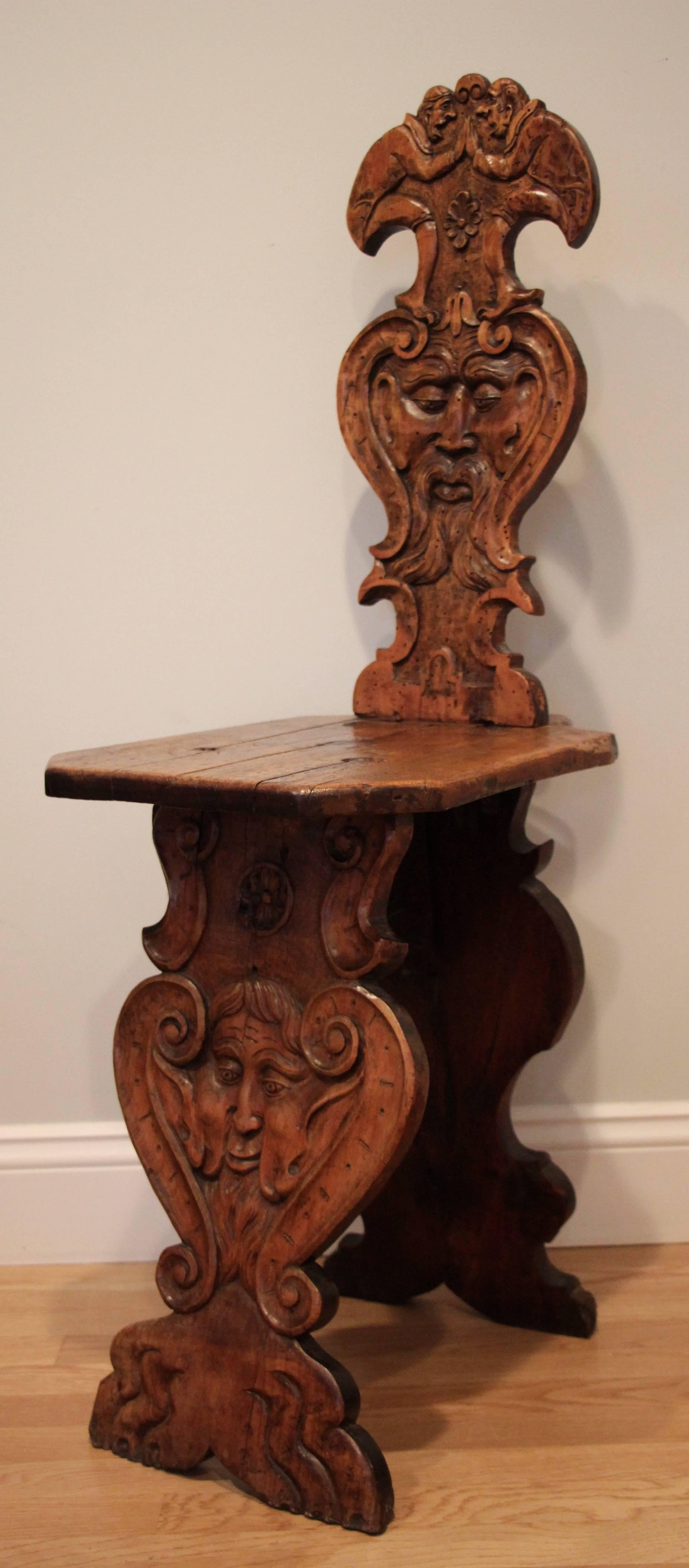 Sgabello chair made of walnut. The back shows a carved grotesque face decoration and two figural decorations, the plank support is decorated with a matching grotesque face mask. The chair was probably reassembled or restored in the 19th century