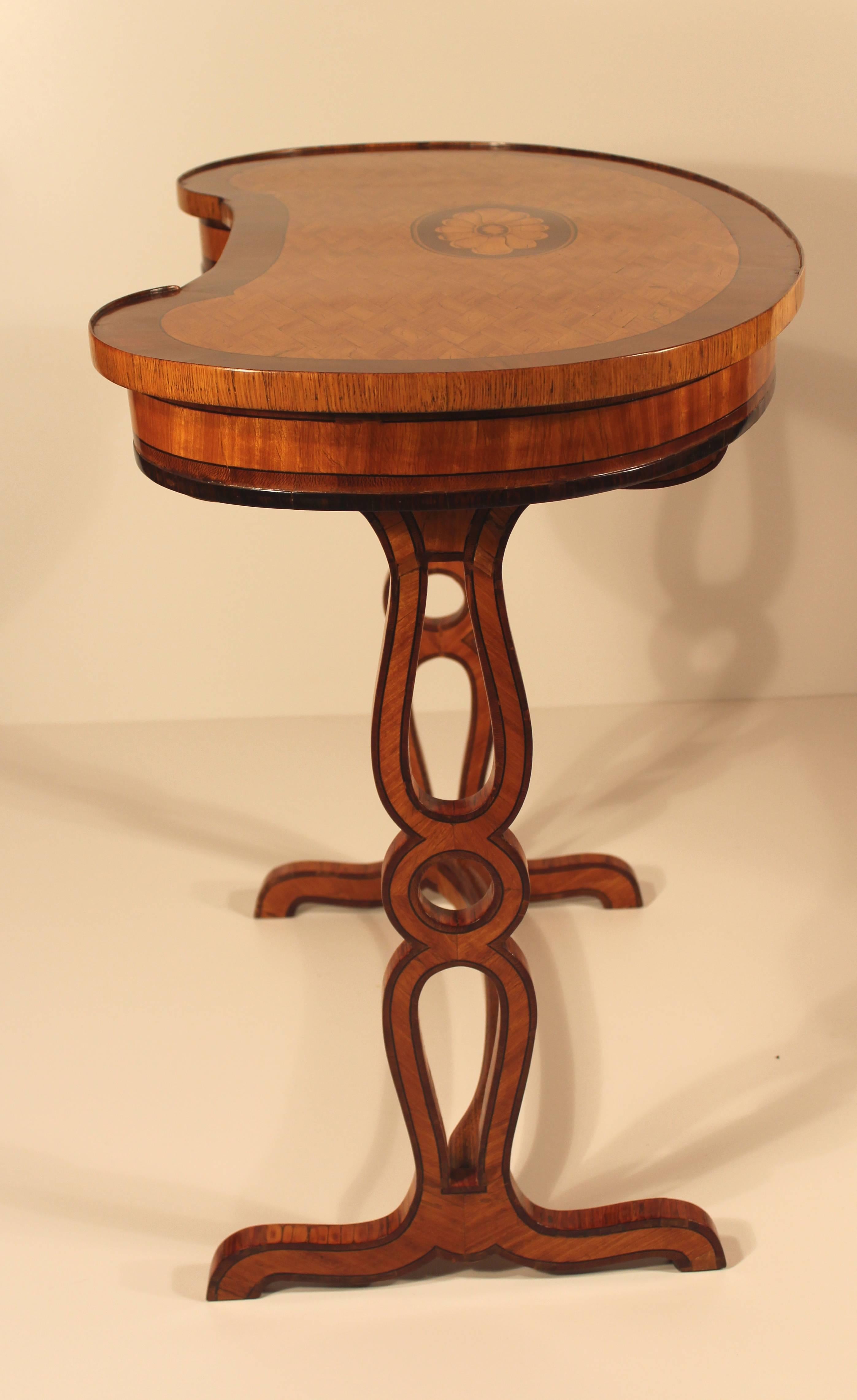 Exquisiter kidneförmiger Tisch aus Kirschbaumholz, Mahagoni und Ulmenholzfurnier, die Platte mit rautenförmiger Intarsienarbeit und einem ovalen Blumenmedaillon. Der Tisch steht auf zwei durchbrochenen Sockeln, die durch eine gerade Strebe