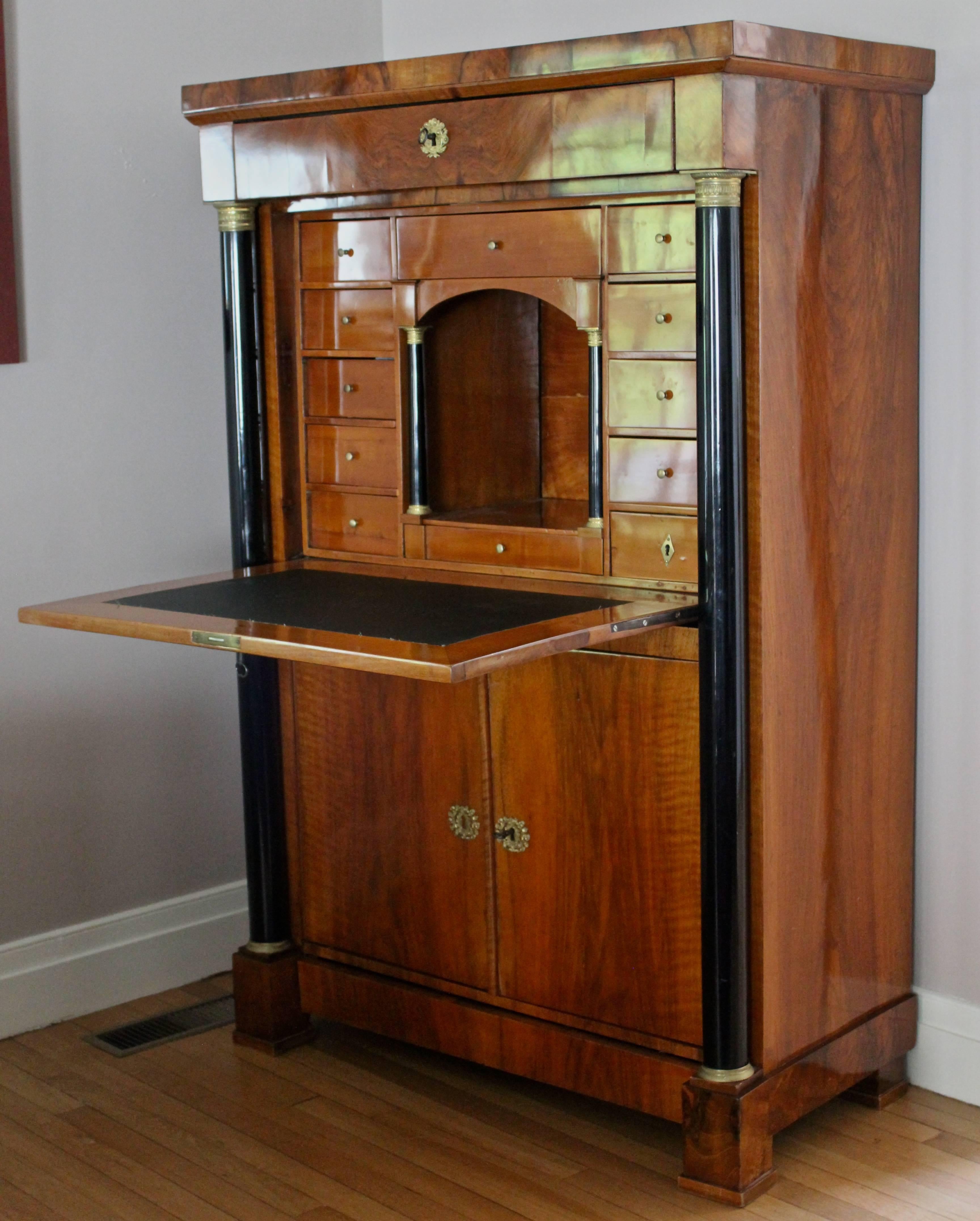 Secretaire a abattant, Germany 1820, Biedermeier period. The outside with fall front and two doors flanked by two ebonized columns shows a beautiful walnut veneer mirrored design. The cherry wood veneered inside opens  to a central compartment