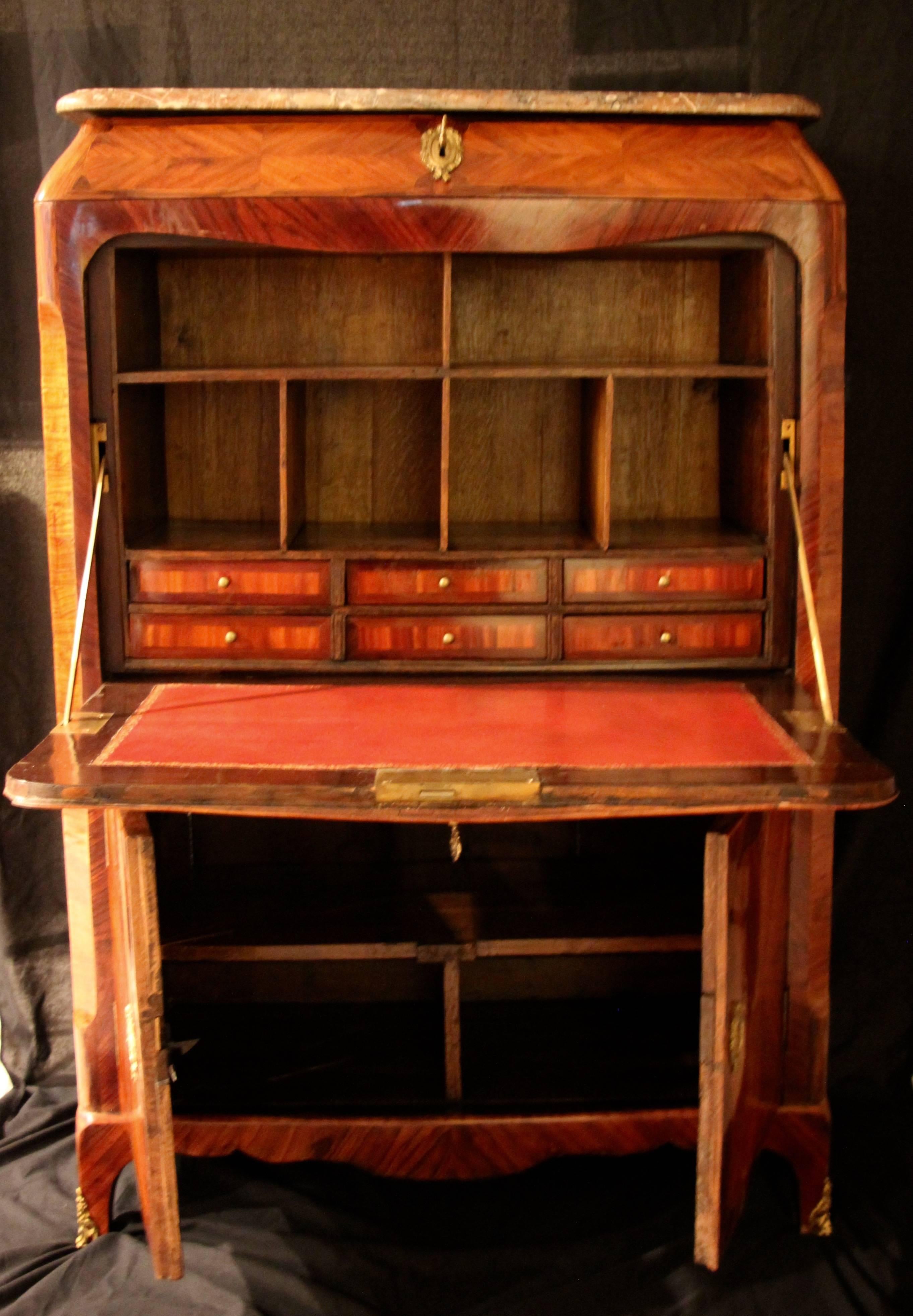Fall top Louis XV secretary, kingwood and rosewood veneer on oak.
The rounded rectangular marble-top above a mirror veneered drawer and a cross banded quarter veneer drop front. Inside are six drawers and six open compartments. The writing surface