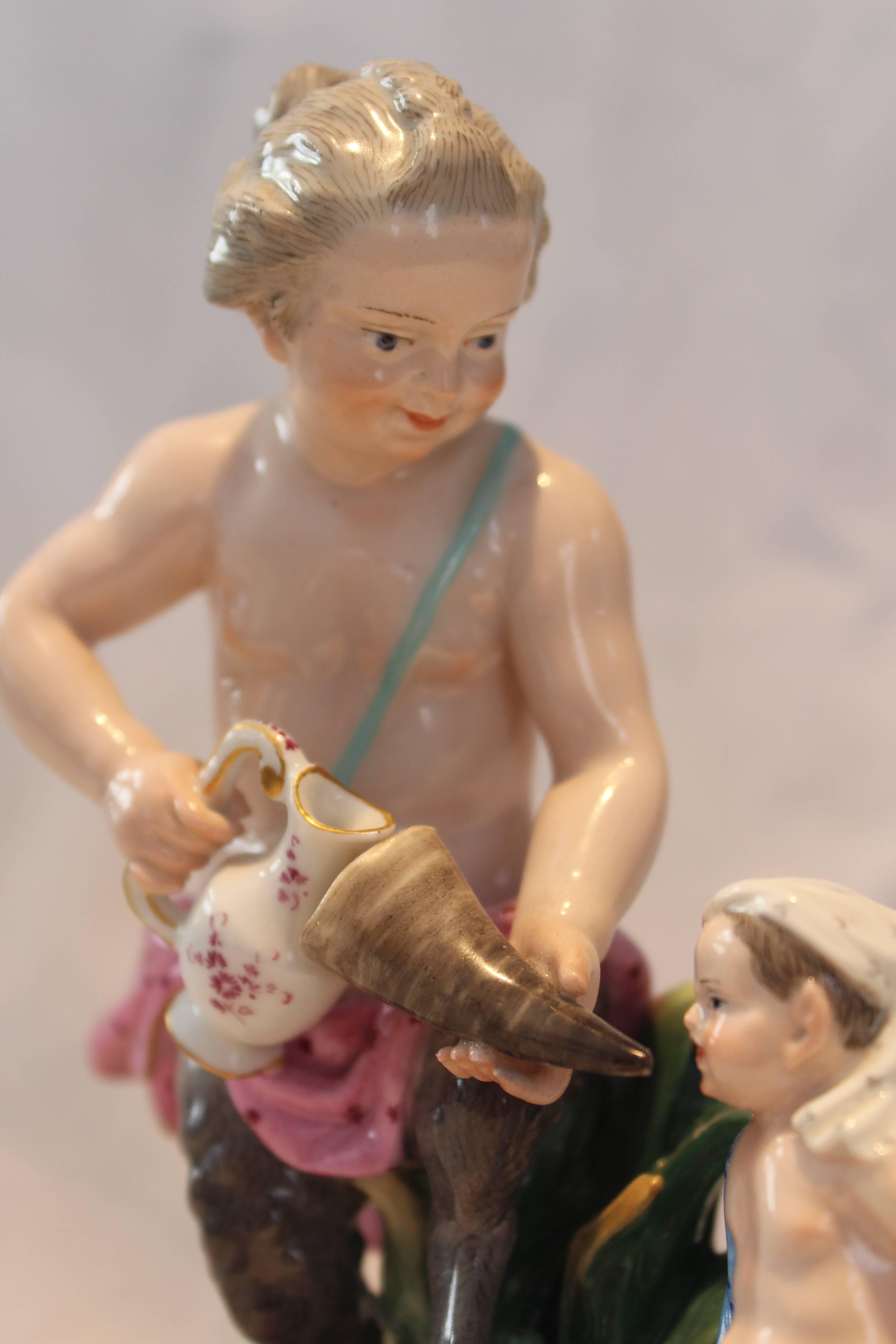Meissen porcelain figure of a faun with her child. The child is sitting on a small chair while his mother is offering him to drink from a horn. Beautiful figure with passion for detail. Underglaze blue sword mark, incised model number D51 / 45,
