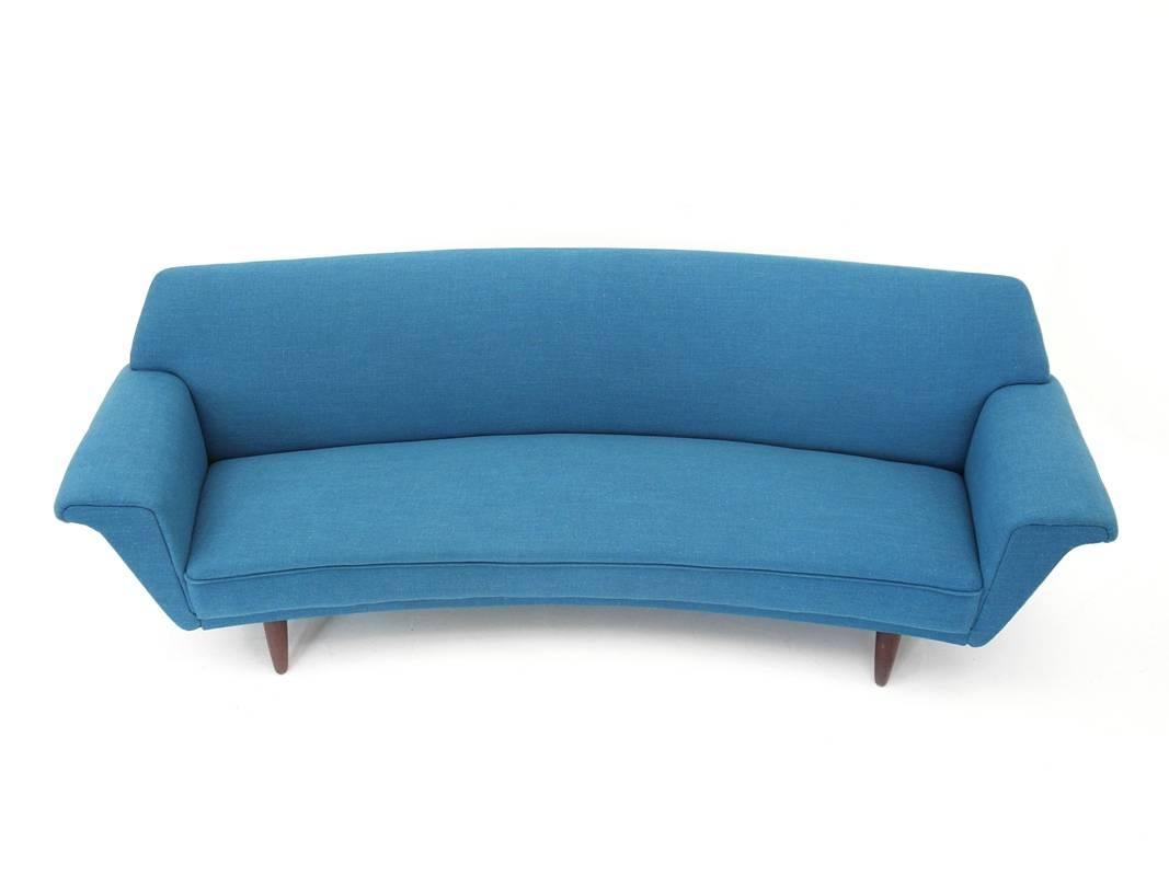 A Mid-Century Modern curved four seat sofa reupholstered in a teal blue fabric, with tapered legs in teakwood, Denmark, 1960s. The sofa displays clean organic design lines from any angle and makes a unique style statement. Although it's large size
