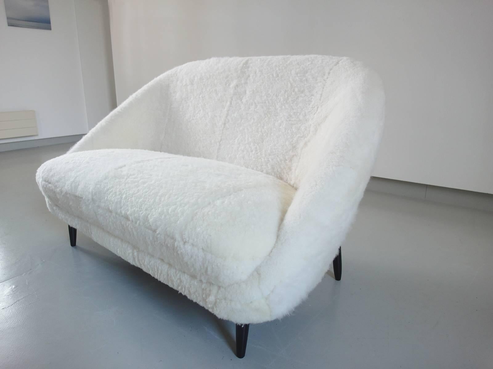 A small sofa or loveseat, Model 115 executed in sheepskin, designed by Theo Ruth for Artifort, Holland, 1959. The sofa is recently reupholstered in a soft and comfortable white sheepskin. 
The black stained beech wooden frame features an elegant