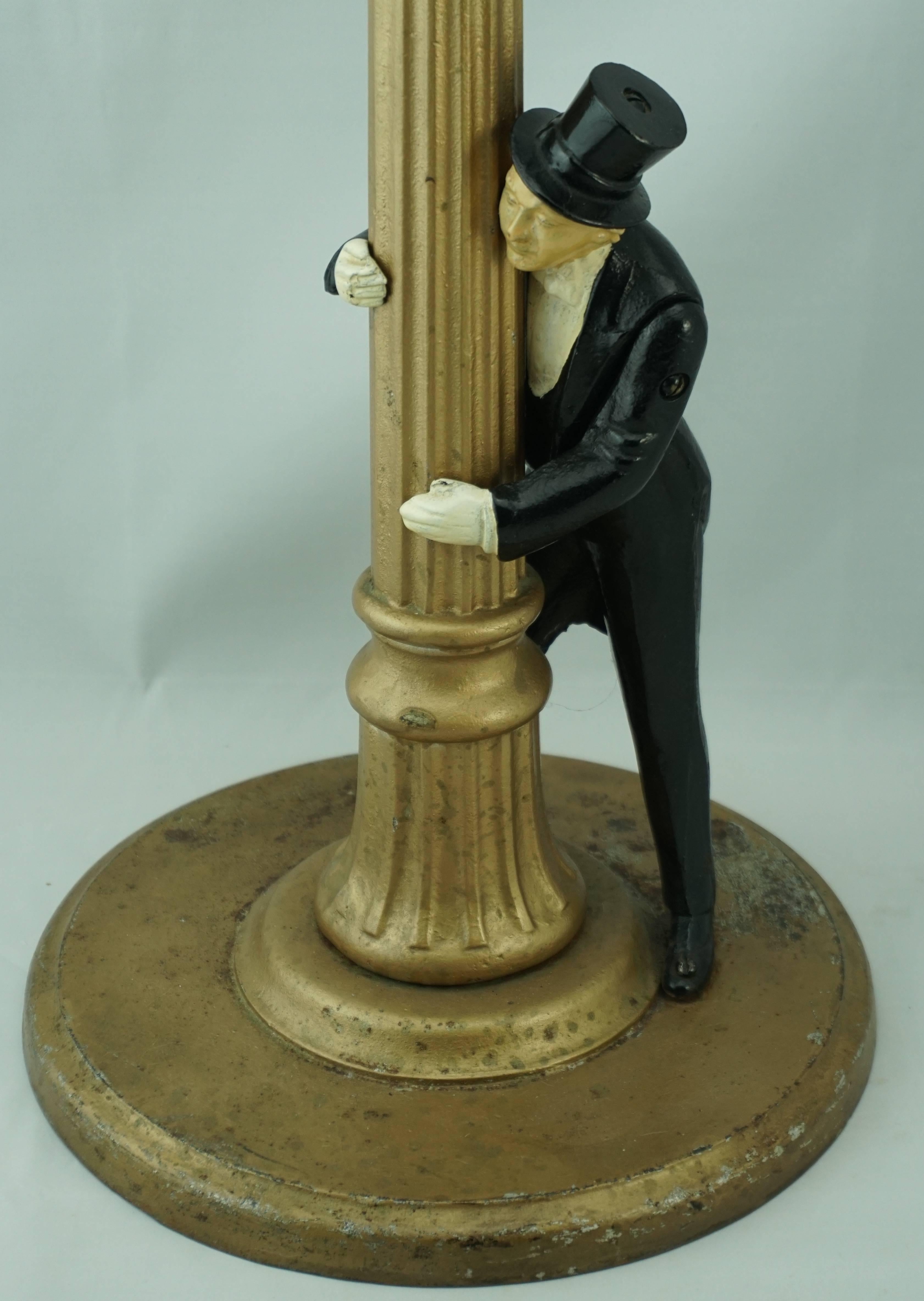 Art Deco American figural cast iron standing ashtray, having a gentleman in top hat and tuxedo tails leaning against the fluted column Stand, with glass ashtray liner. The base marked, 