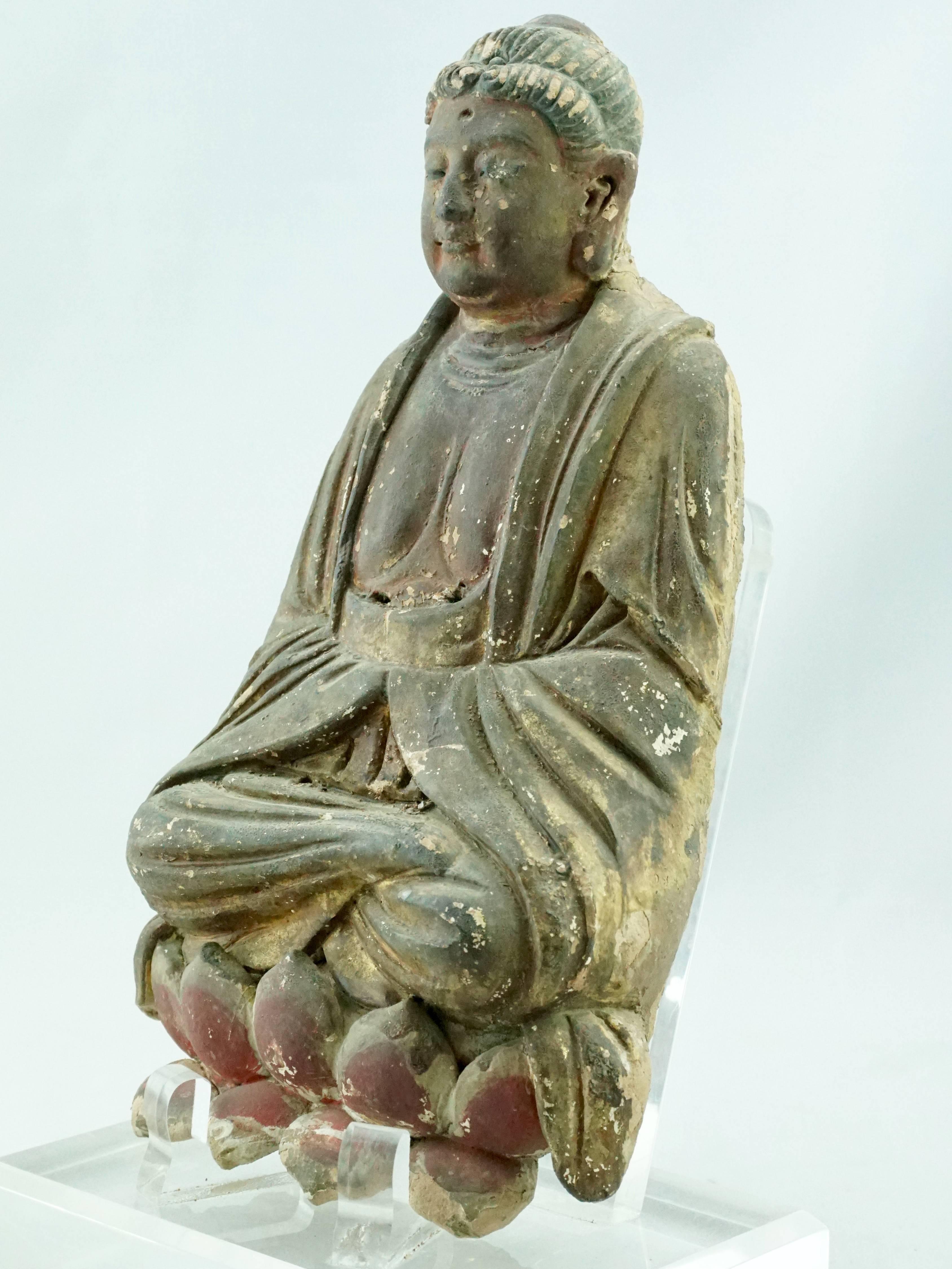 A very fine late Yuan to early Ming Chinese terracotta gilt and polychrome painted Buddha figure, he is dressed in thick robes, his hair arranged in typical early song or Yuan dynasty style and he is sitting on a colorful red lotus flower.
This
