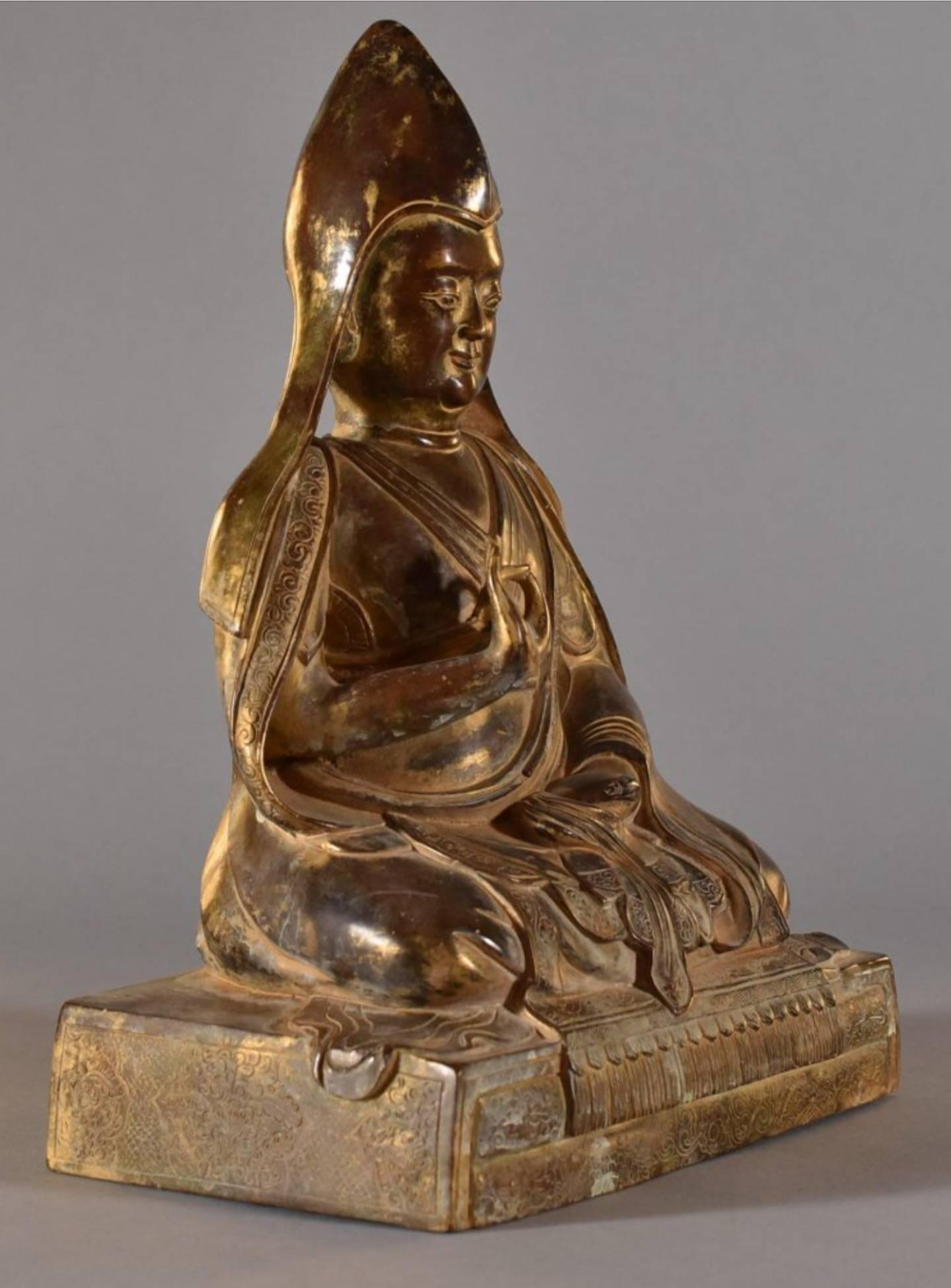 A Sino-Tibetan gilt bronze seated figure of a lama, Tsongkhapa, Chinese Qing dynasty, 18th century. 
The large and magnificent figure is seated on a rectangular pedestal base with legs crossed in dhyanasana, one hand held in vitarka mudra and the