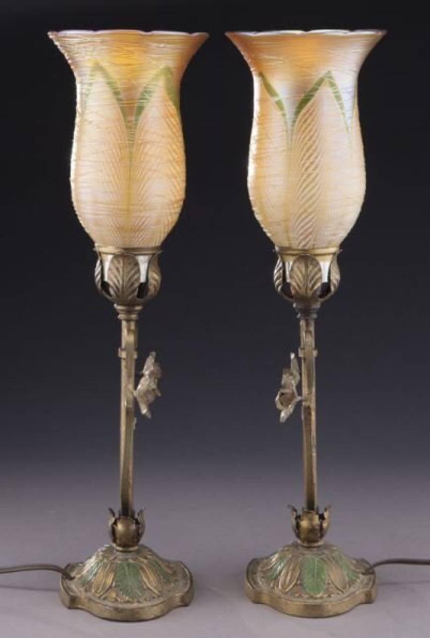 Pair of Durand art glass mantel lamps, iridescent gold shades with white pulled feathers and overall threading, floral embossed Art Nouveau stands with green enameled leaves. Electrified. 

Measures: 17