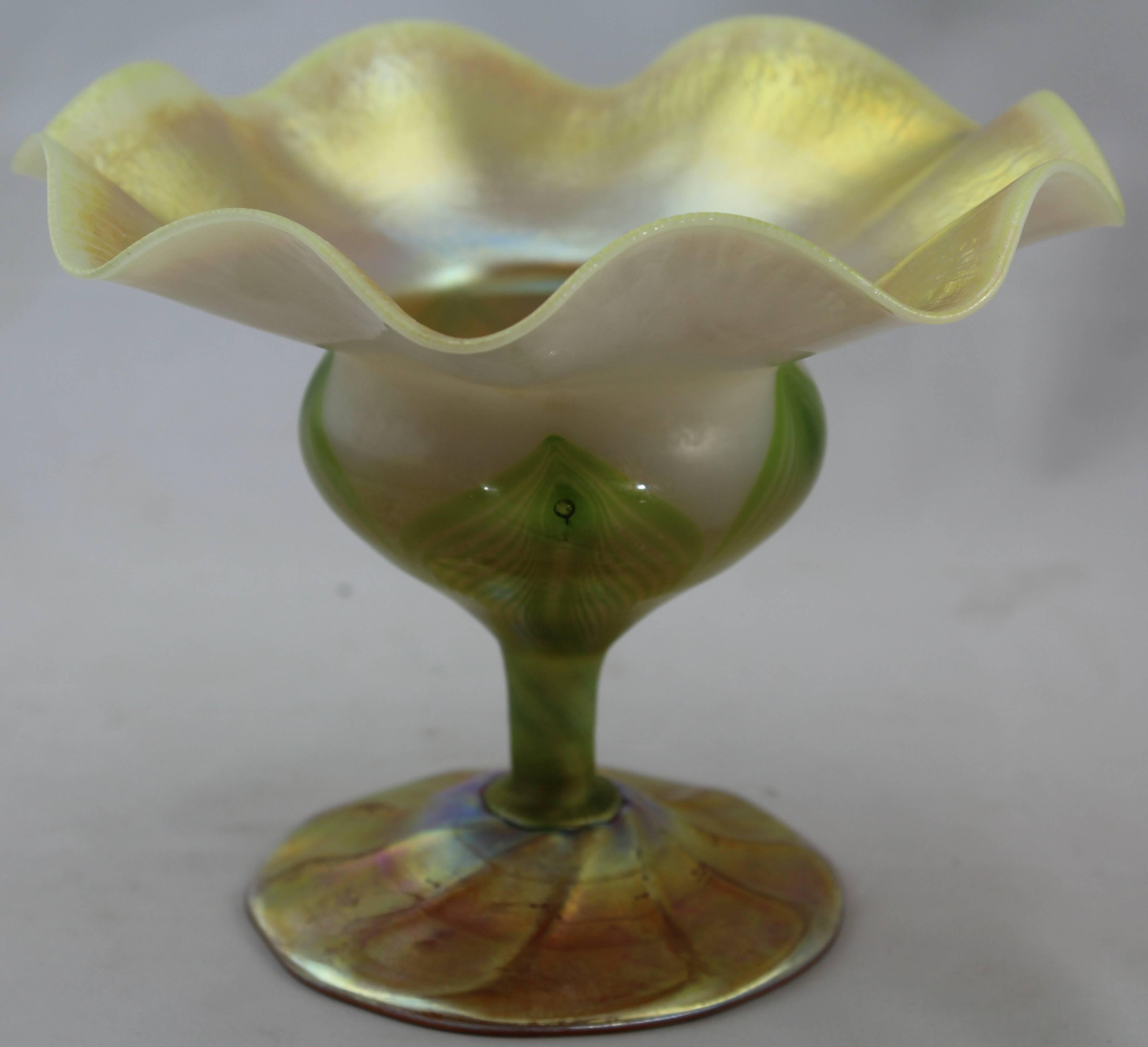 Tiffany Studios feather-pulled gold favrile glass floriform vase,
circa 1909. Engraved L.C. Tiffany - Favrile, 858 D.
Measures: Ht. 5-1/2 in.
From the estate of Helen Bentley. 

Condition Report*:

Attractive onion skin texture to the lip rim