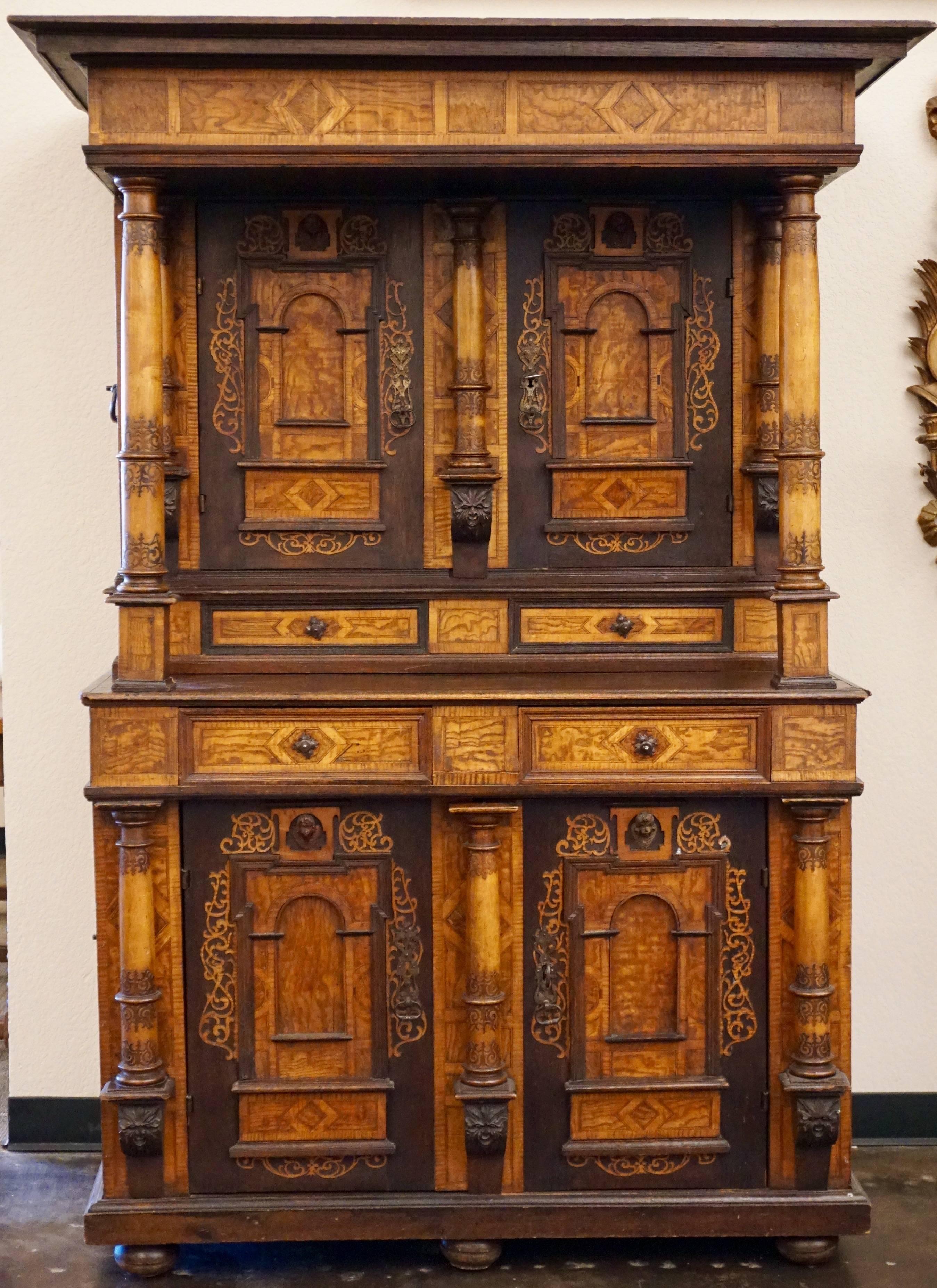 Rare 18th-19th century Alsacienne inlaid cabinet, the stepped inlaid cornice on columnar supports over two doors with architectural panels surmounted by putti masks above similar two-door base, upper and lower sections revealing shelved interiors,