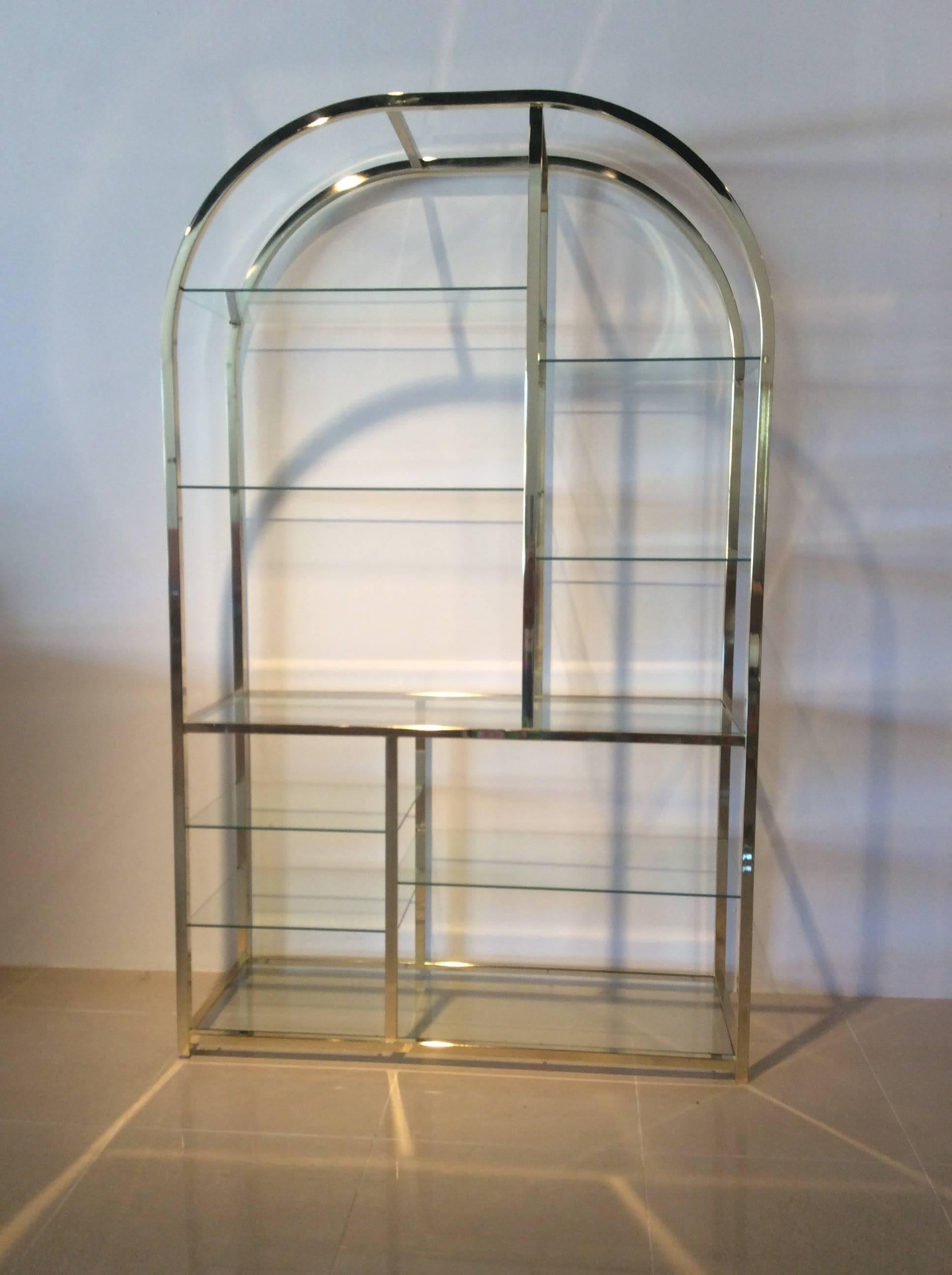 Vintage Hollywood Palm Beach Regency DIA Design Institute of America DIA arched brass etagere display shelf. Tagged DIA and pictured. On one side there is a few patina spots that are pictured. Includes nine glass shelves as pictured. 