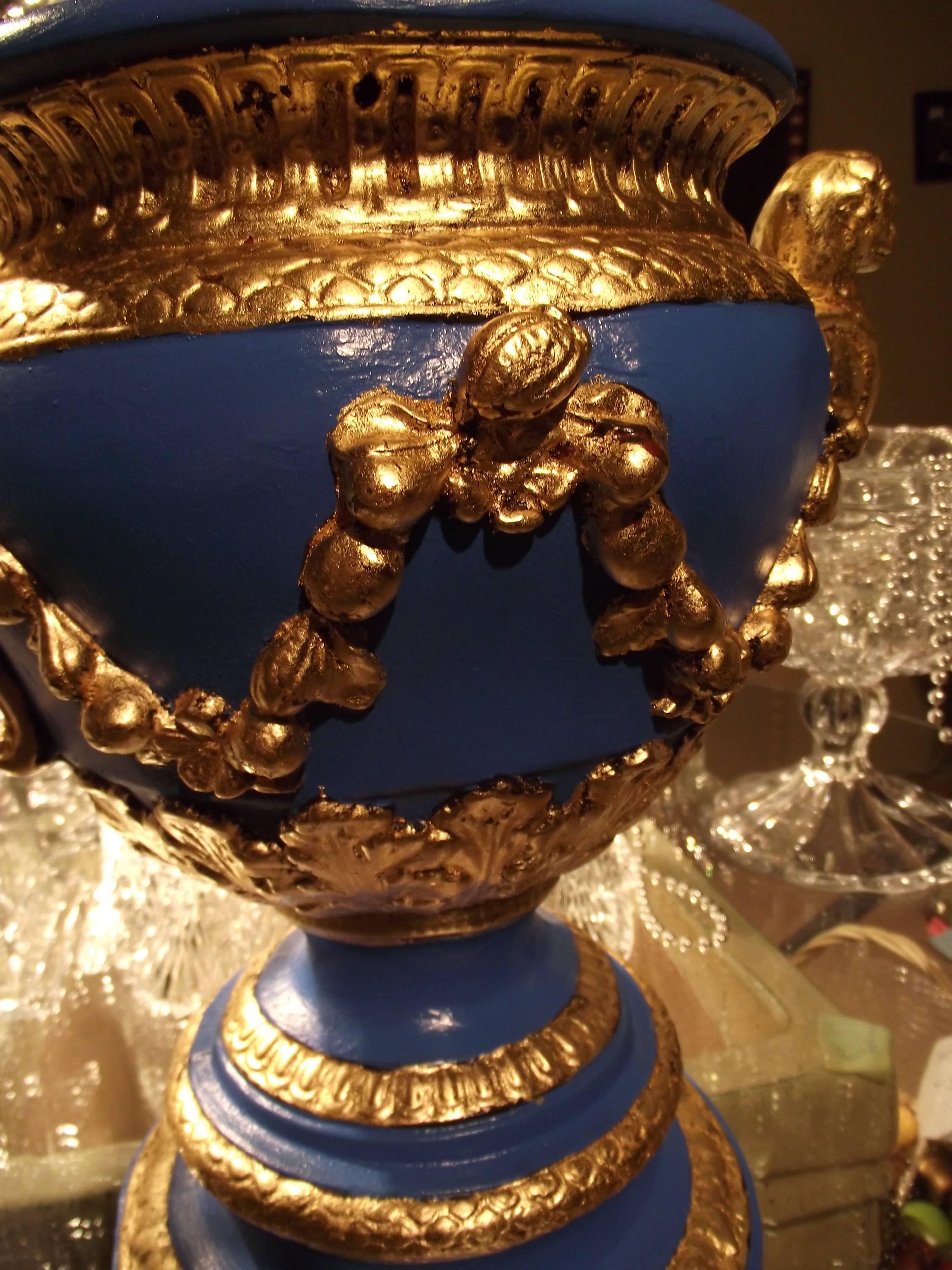 This striking reproduction plaster urn has an original hand applied finish produced in my studio. The gold leaf foil was hand applied.
The handles are ornamented with a lion head.
It stands 15" tall is 12 1/2" wide and 10"