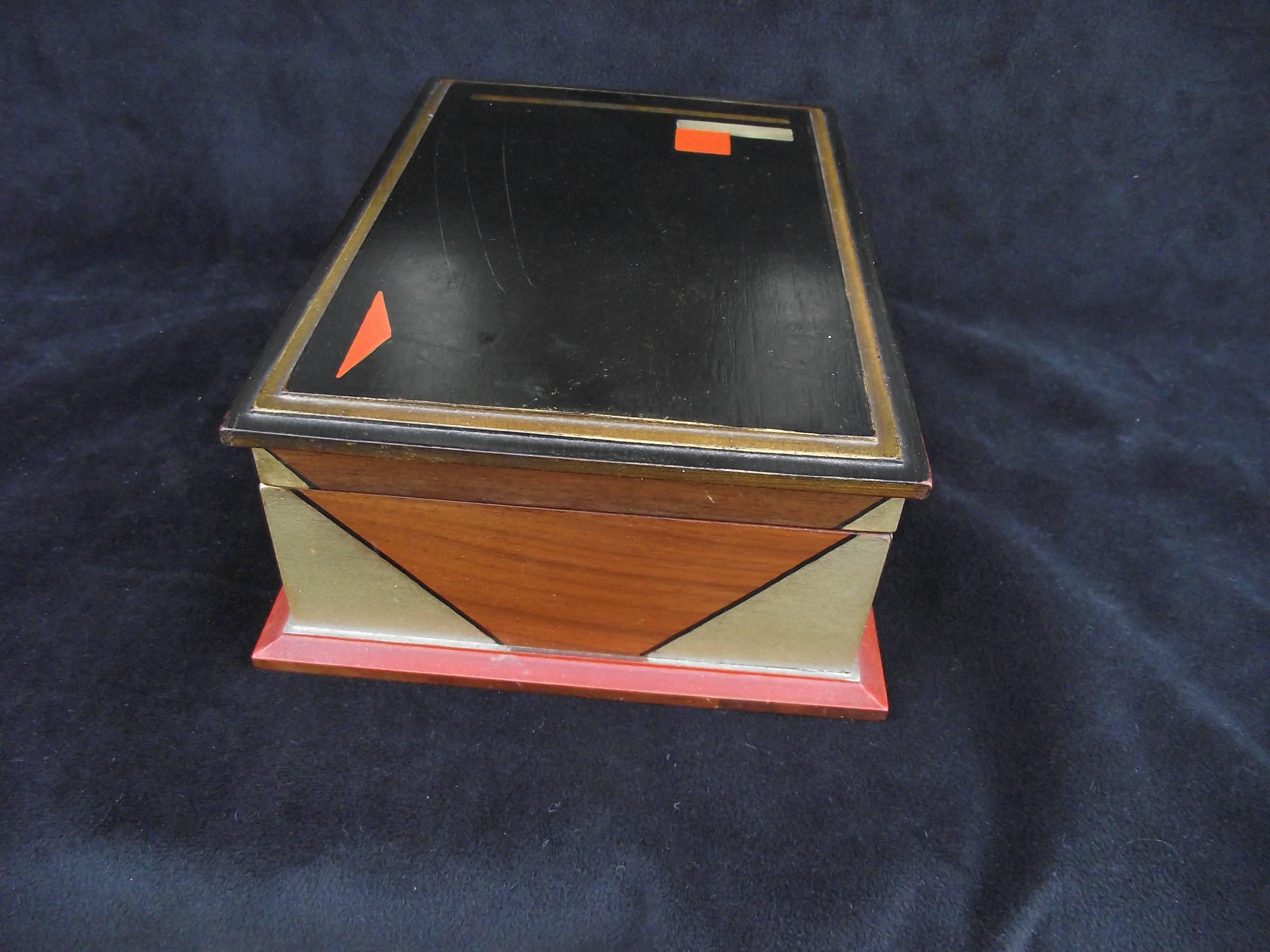 This rare hand-painted Art Deco box features two shades of gold metallic trim. It has tow red accents on top and a more muted red trim around the bottom edge.