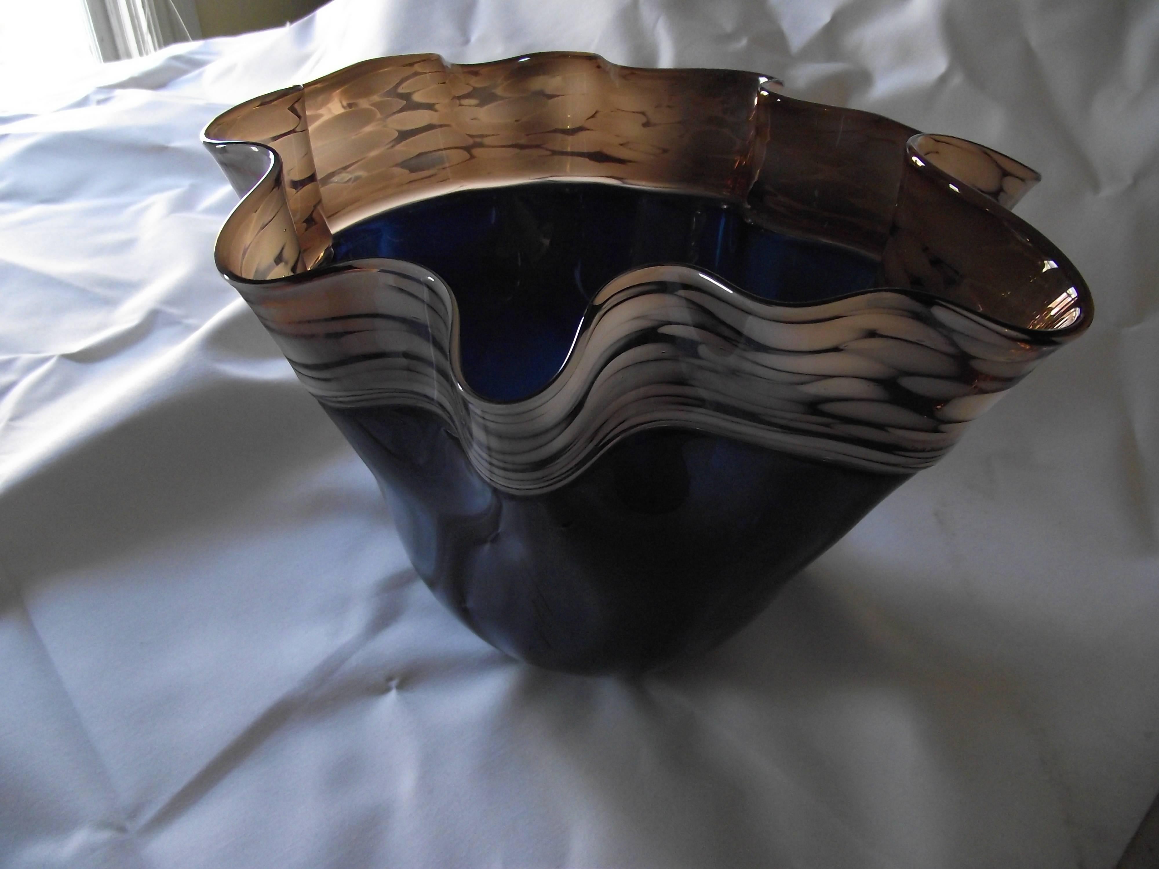 This handkerchief style bowl is a rich blue glass with an interesting brown trim. 

Even with its free-form design it has the bowl as a distinct elegance all its own.