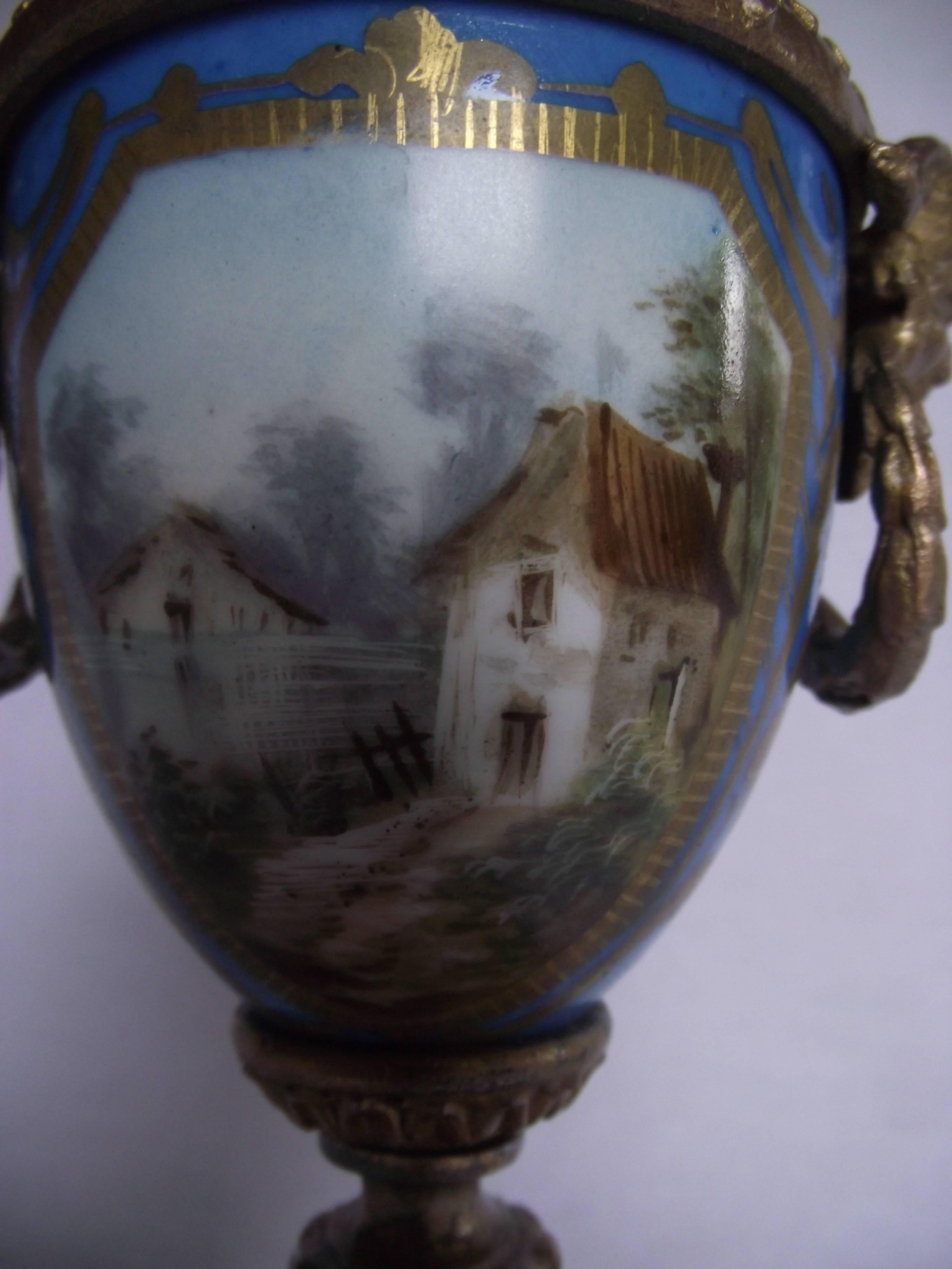 Beautiful little Sèvres style gilt metal scenic hand-painted porcelain urn. Side mounts feature a Sartre face and wreath. A very distinctive piece for a book shelf or tabletop.
