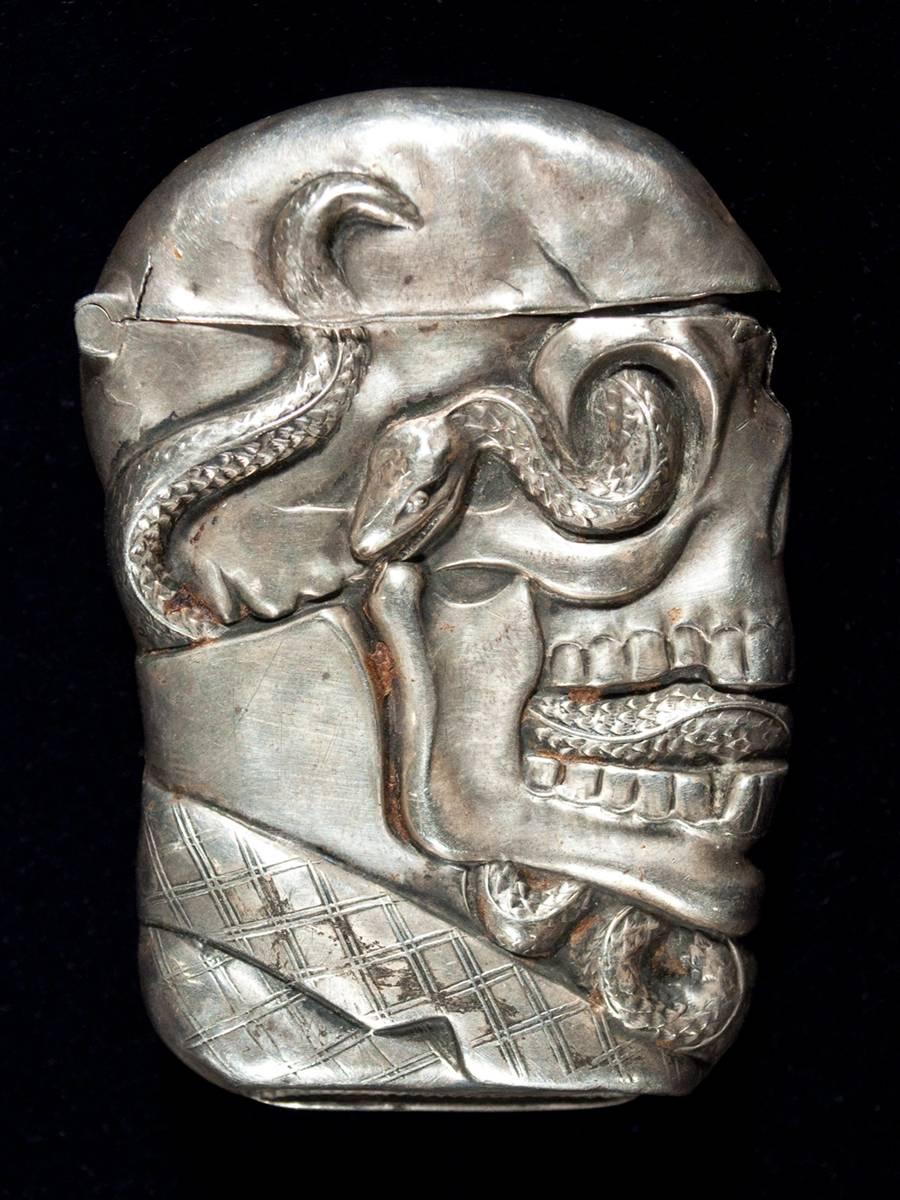 Offered by Zena Kruzick.
Late 19th century sterling silver skull and serpent match safe (Vesta).
Unknown manufacturer.

This rare match safe is marked sterling with a pinched striker on the bottom. A serpent winds through a dapper skull's eye
