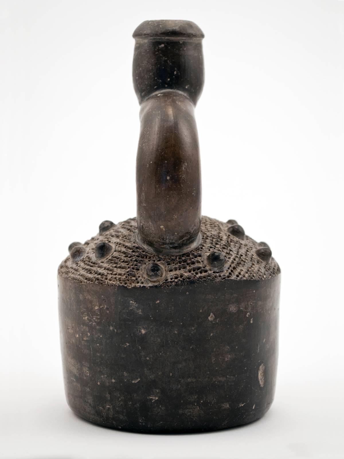 Offered by ZENA KRUZICK
Pre-Columbian Chavin Blackware Stirrup Vessel 
A classic blackware stirrup vessel with picked and knobbed surface. This piece is from the Chavin culture, Tembladera phase, ca. 700-400 B.C.  Stirrup spout vessels were a