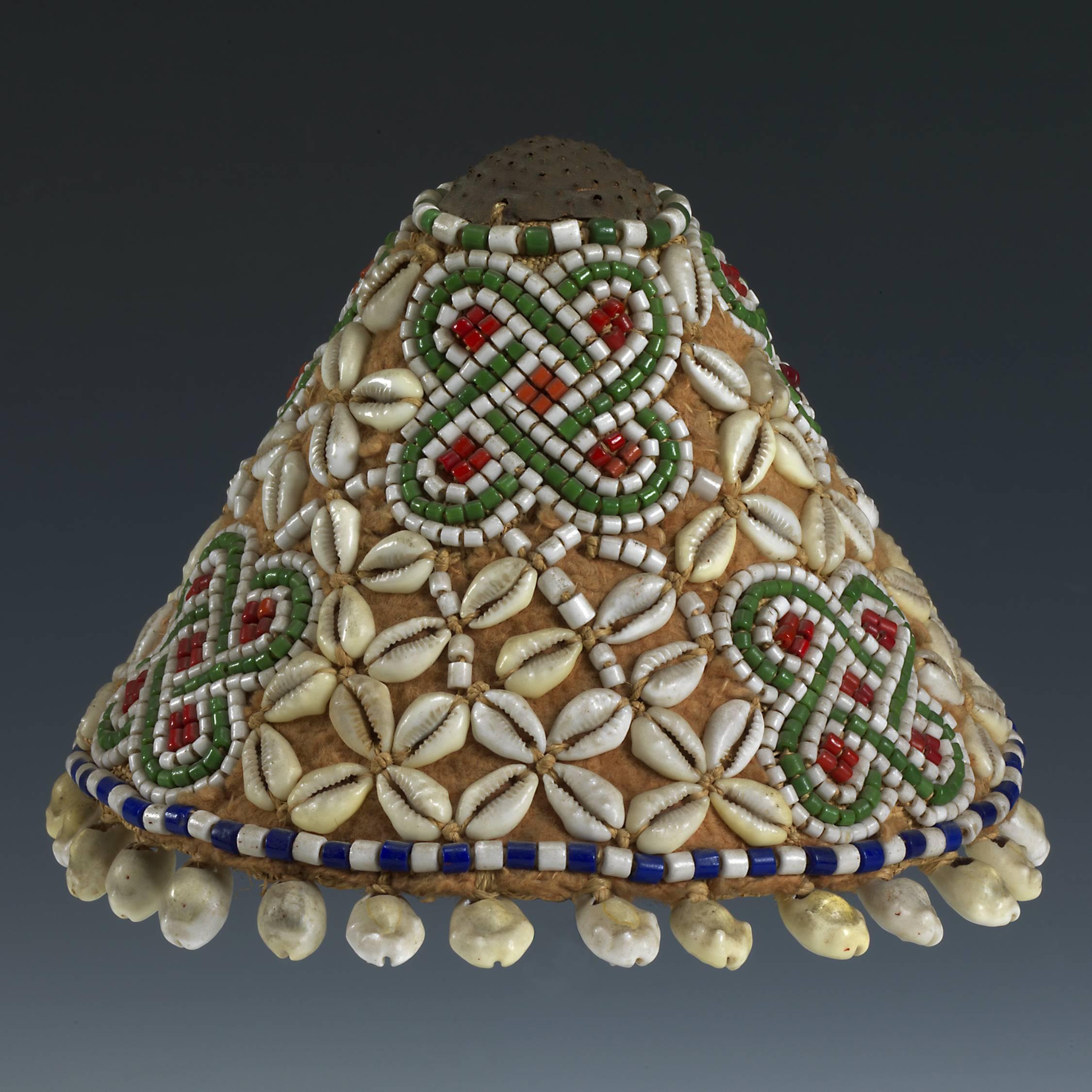 Offered by Andres Moraga
ceremonial hat.
Made for the Bushoong ruling elite of the Kuba Kingdom in D.R.Congo.
Over a base of raffia, decorated with glass beads, copper, cowrie shells and barkcloth. The blue, white, green and red trade beads date