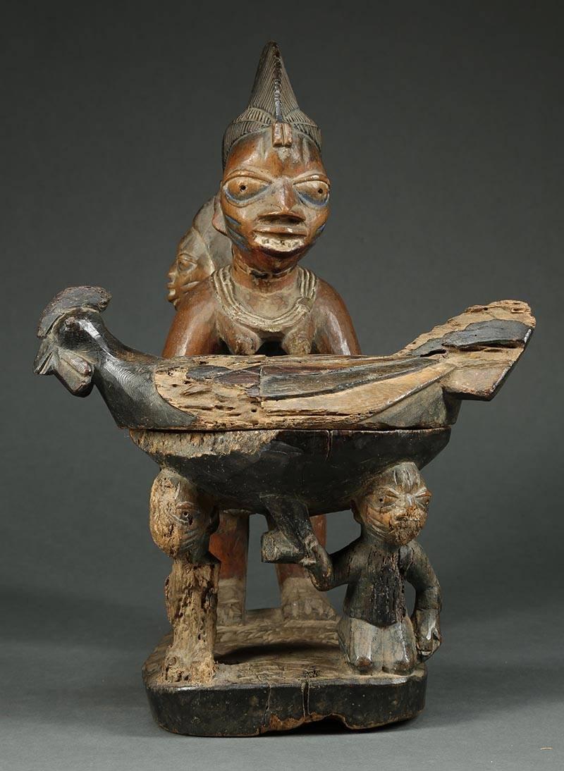Blessed by time, an early beautiful Yoruba female figure with baby riding on back, presenting an offering bowl in the form of a chicken with a removable top. Great Yoruba mother's face with scarifications and an excited baby. Areas of heavy wear,