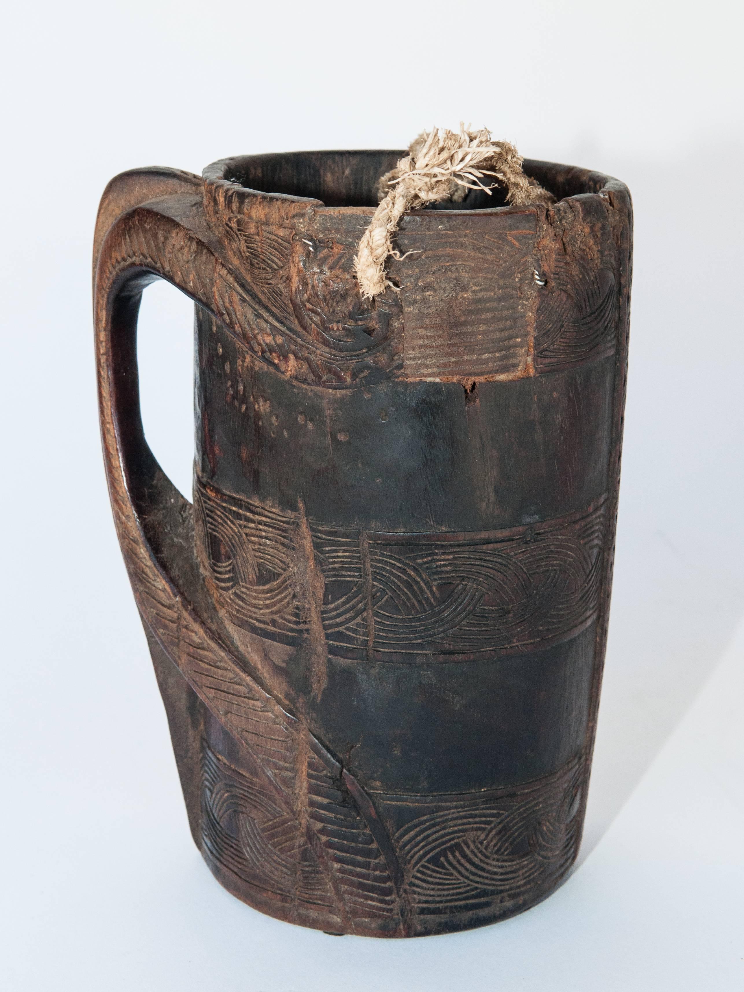 Wooden Carved Milk Pot with Stylized Monkey Motif. Mid-Late 20th Century. From the Middle Hills of West Nepal.
This rustic milk pot was hand carved of local hardwood in the middle hills of western Nepal,  using very basic tools. Geometric designs