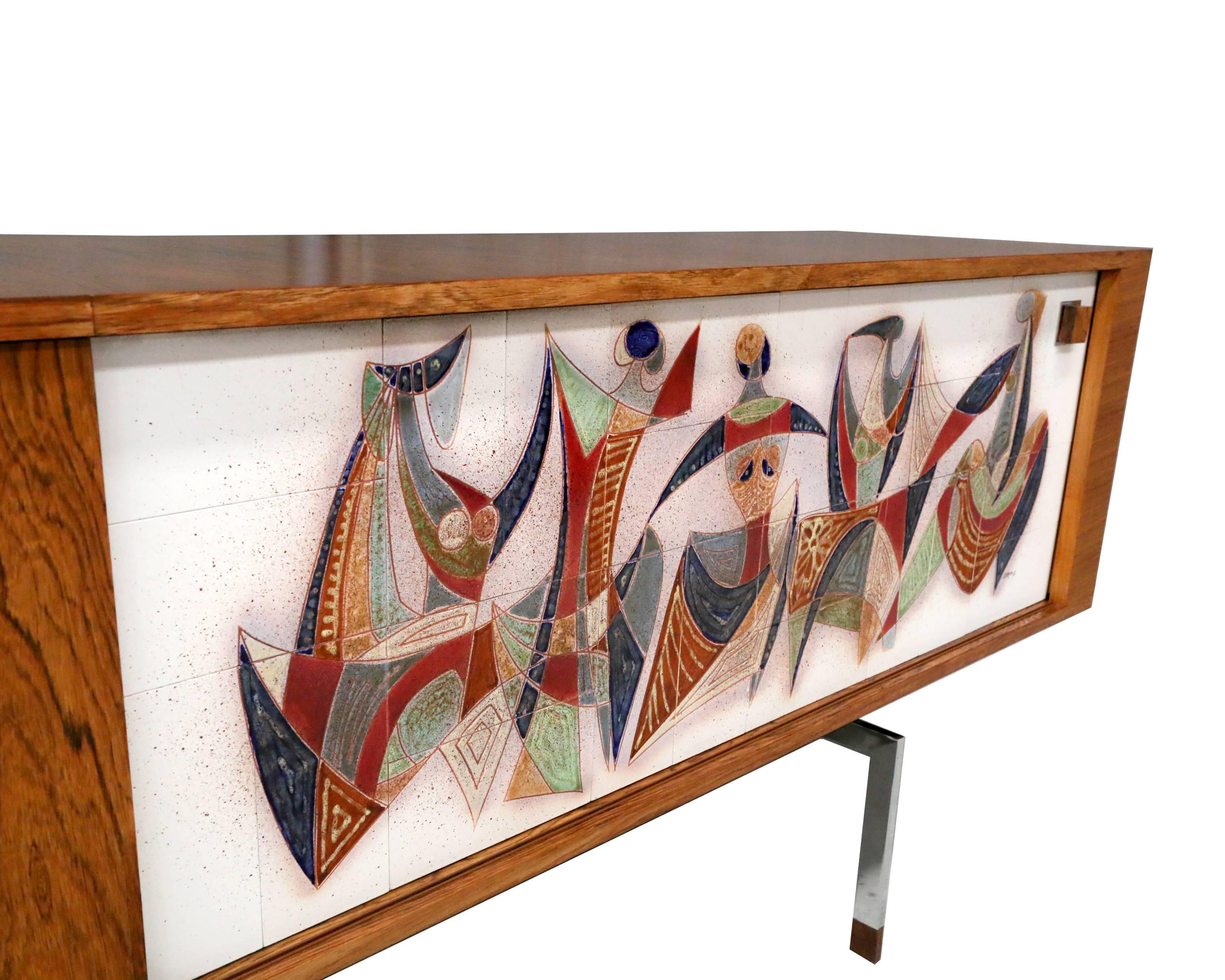 Vintage Belgian modernist sideboard with two sliding door panels, one in teak veneer and one in modernist ceramic art tiles. The sideboard is 260cm long.
Difficult to find. More items from this designer in my other listings.

We can offer