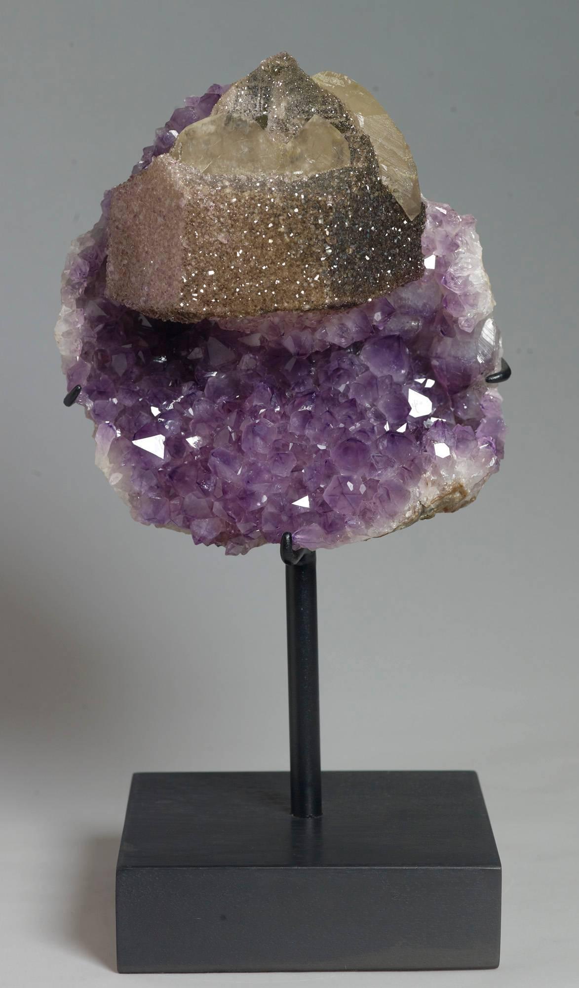 A large hexagonal crystal of calcite covered with goethite included amethyst crystals on a background of larger amethyst crystals. Measures: 36 x 18 x 15 with stand.