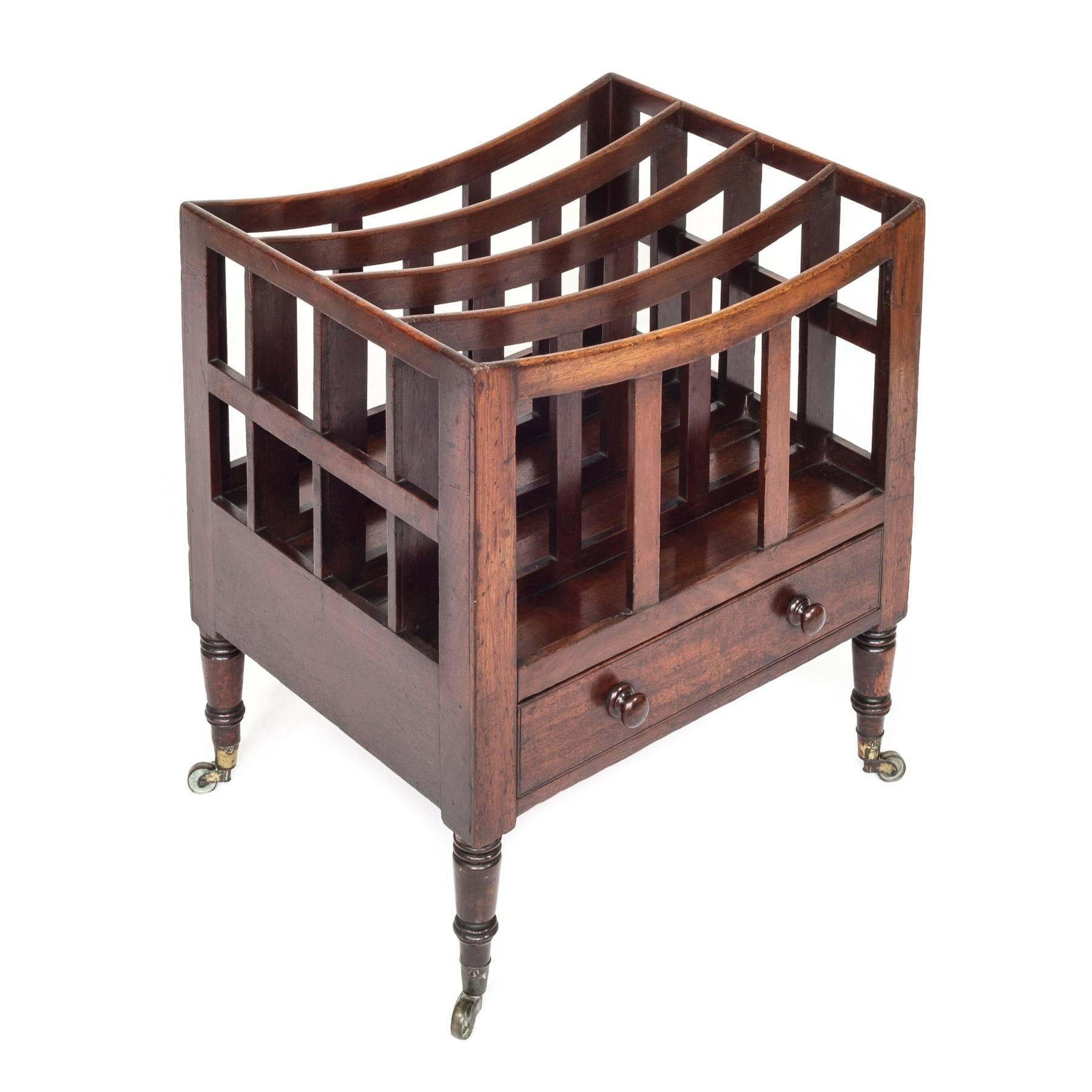 A fine and well proportioned late George III - early Regency mahogany Canterbury, with four curved divisions above a frieze drawer, supported on four ring-turned tapering legs, ending in original brass castors. The drawer is hand dovetailed and