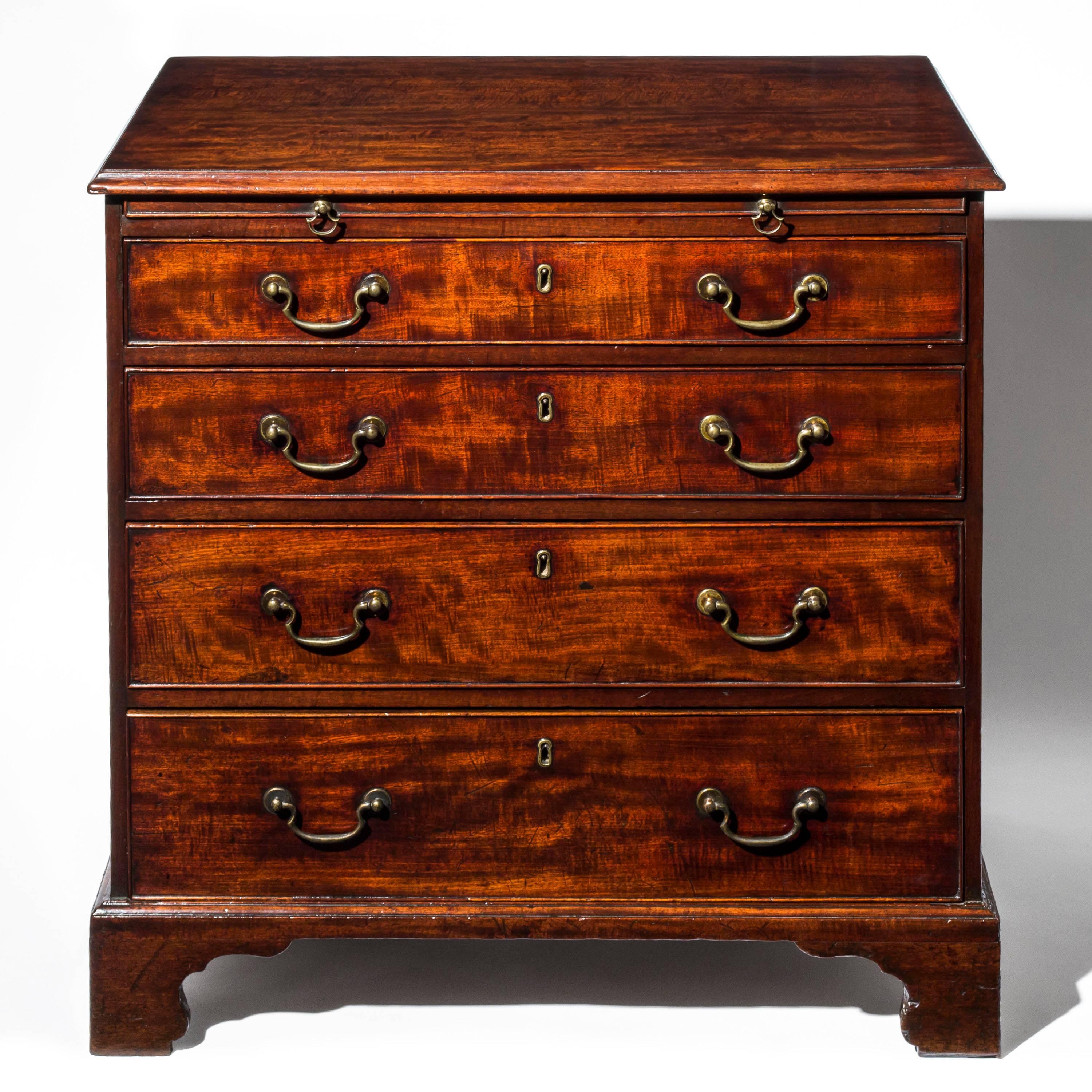 A fine English George III Chippendale period chest of drawers, of pleasing color and desirable compact proportions

circa 1770.

The rectangular top with applied moulded edge, over a brushing slide with brass axe head pull handles, above an