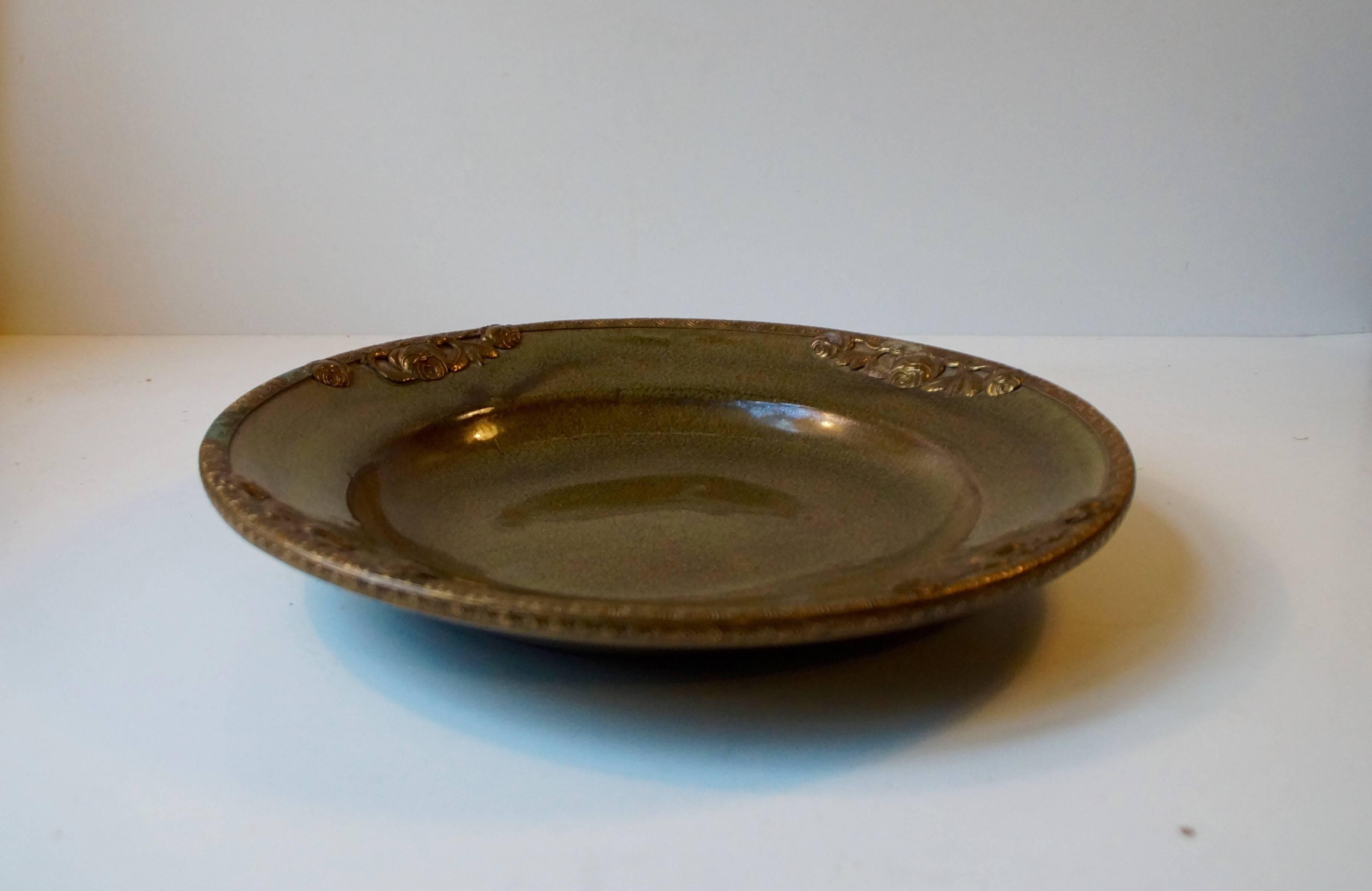 Rare decorative dish for fruit manufactured by Michael Andersen in Denmark, circa 1910. It has a rich and deep dark green glaze with nuances of different colors. The Perimeter is decorated with floral impression set in patinated brass.