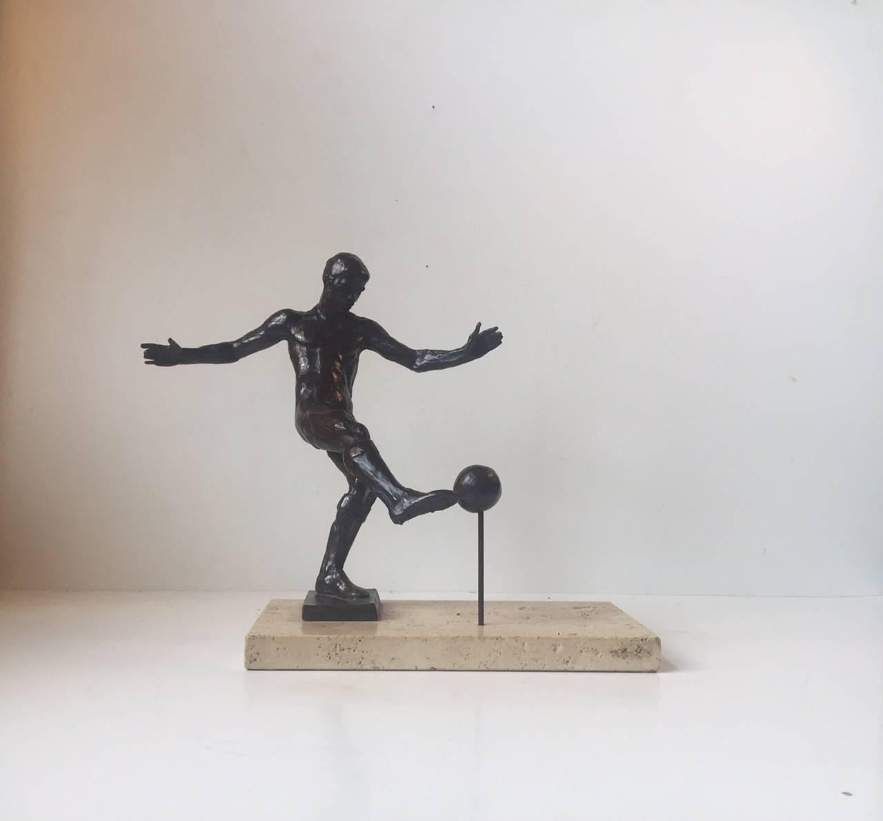 Detailed bronze sculpture depicting football player kicking to the ball. It is mounted on an Italian travertine base. It is commissioned by Royal Copenhagen in Denmark relation to the Olympic Games in Montreal in 1976. The sculptor is