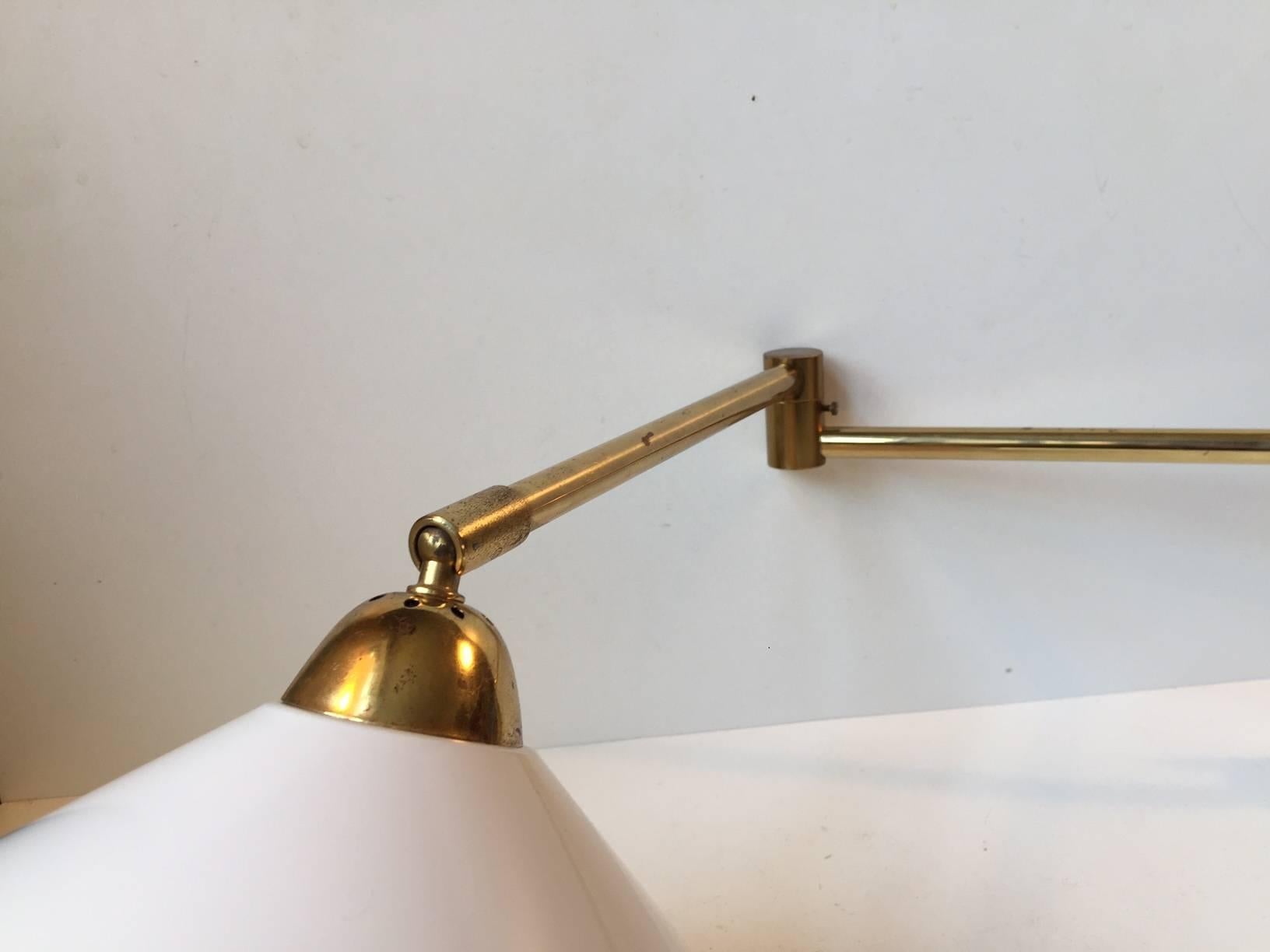 Swing-arm brass wall light with articulated joints and large white conical shade. Designed by Bent Nordsted and manufactured by Lyskjær Belysning in Denmark during the 1960s. The total reach of the light is 70 cm (28 inches, approximate). Maker mark