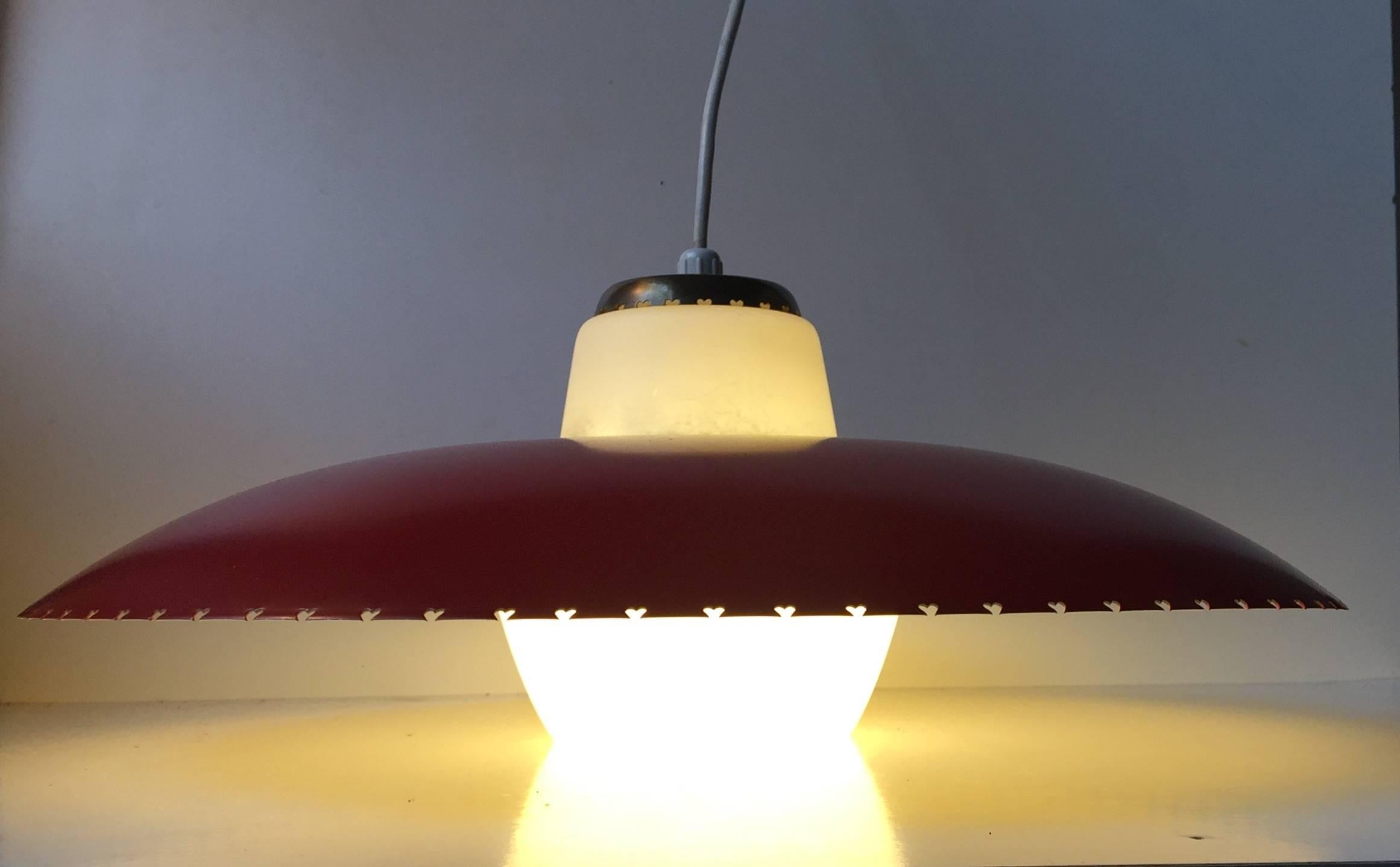 Danish ceiling light designed by Bent Karlby for Lyfa, Denmark and manufactured in the late 1950s. The light consists of a large red lacquered shade with perforated hearts to the edge, solid brass details and a bell clock shaped opaline glass center.