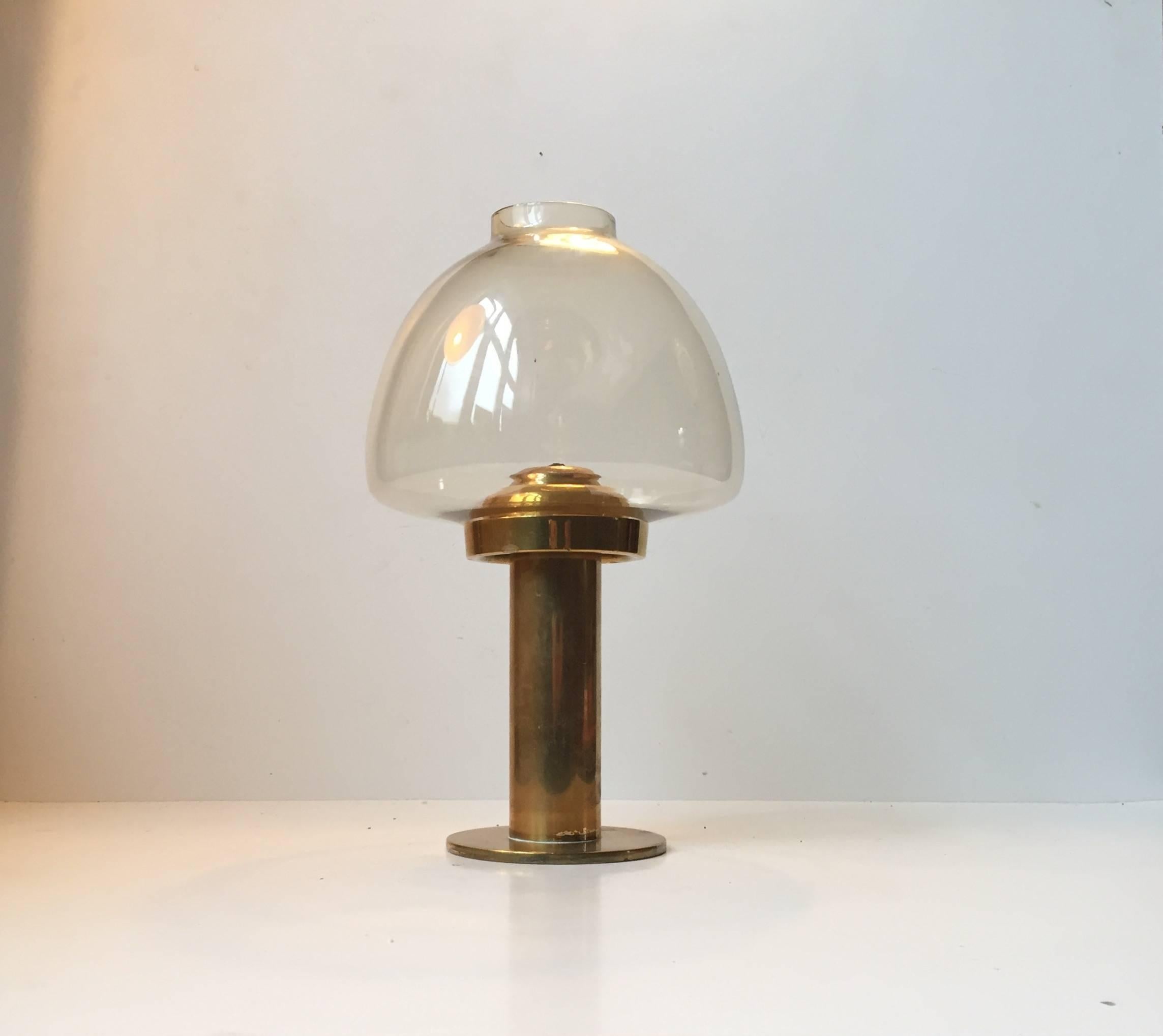 This candleholder Model L102 features a mouth-blown smoked hurricane glass shade and a brass base with a spring mechanism that pushes up the candle while it burns. This piece was designed by Hans Agne Jakobsson and manufactured by Markaryd AB. The