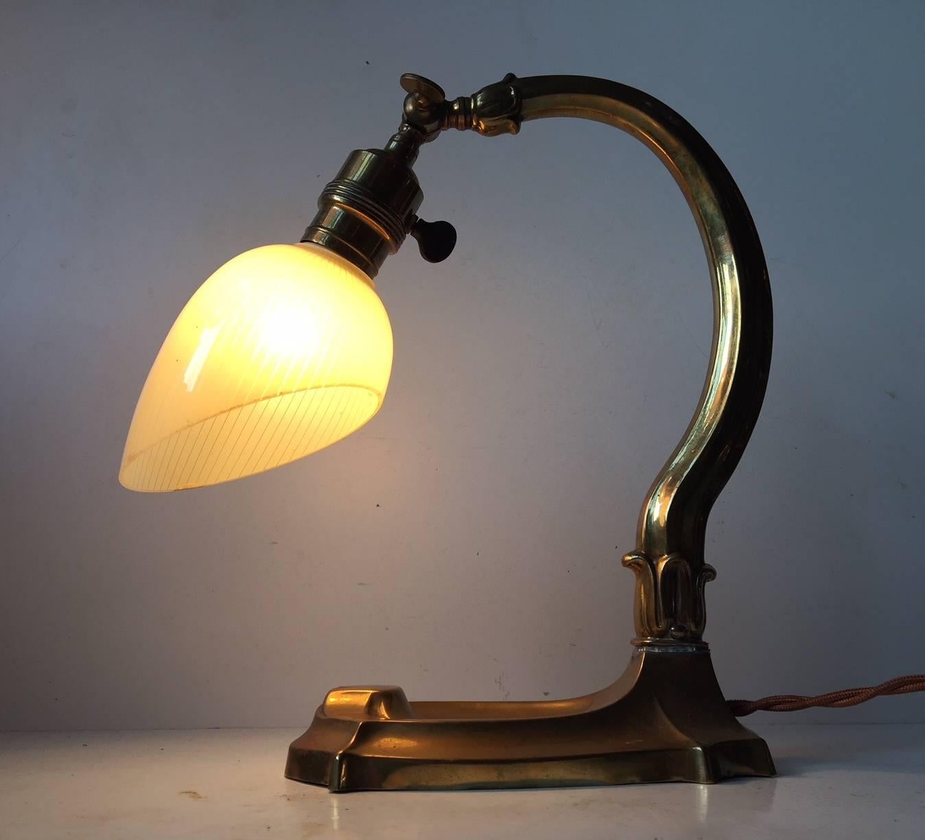 This Danish 1920s desk lamp has a solid brass frame and base. It is mounted with a pin-striped, single-layered glass shade. Adjustable at the shade - 180 degrees.