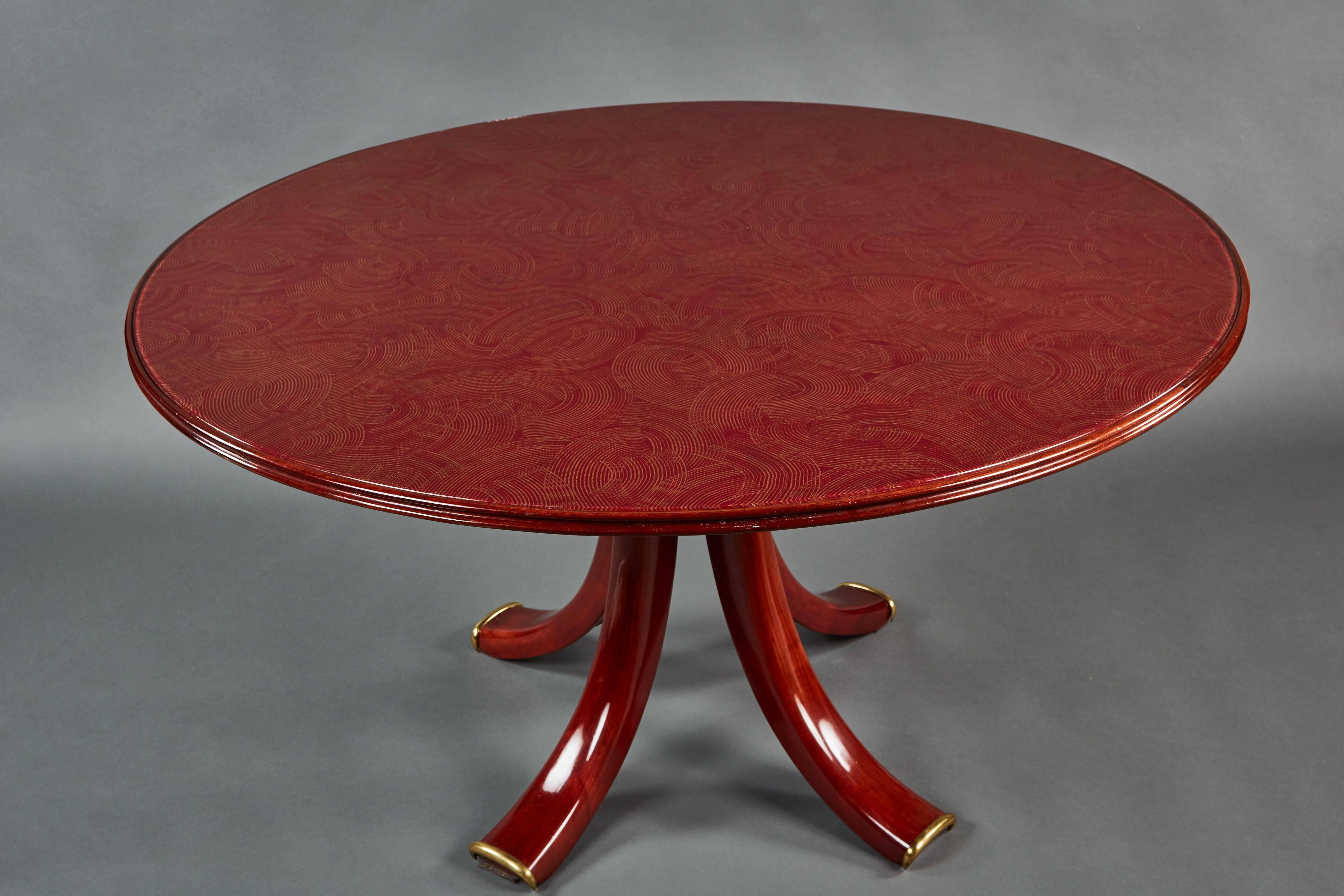 An exquisite and rare round Osvaldo Borsani table. The top is of an elegantly under-painted burgandy glass with a swirling pointillist design in gold. The mahogany lacquered base is finished with brass sabots.