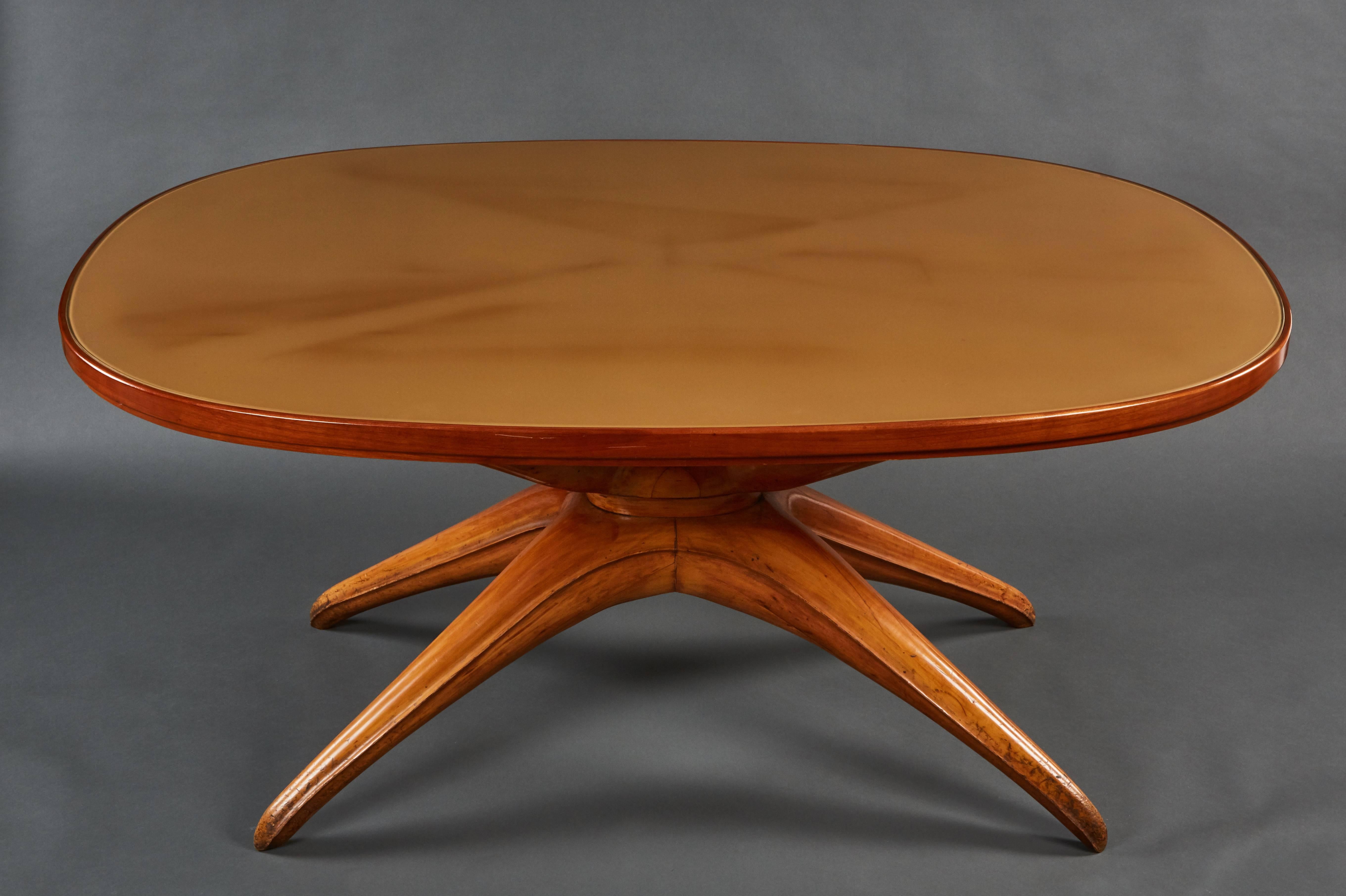A dramatic oval table attributed to Osvaldo Borsani, featuring a significant sculptural wooden base and gold painted glass top.
 