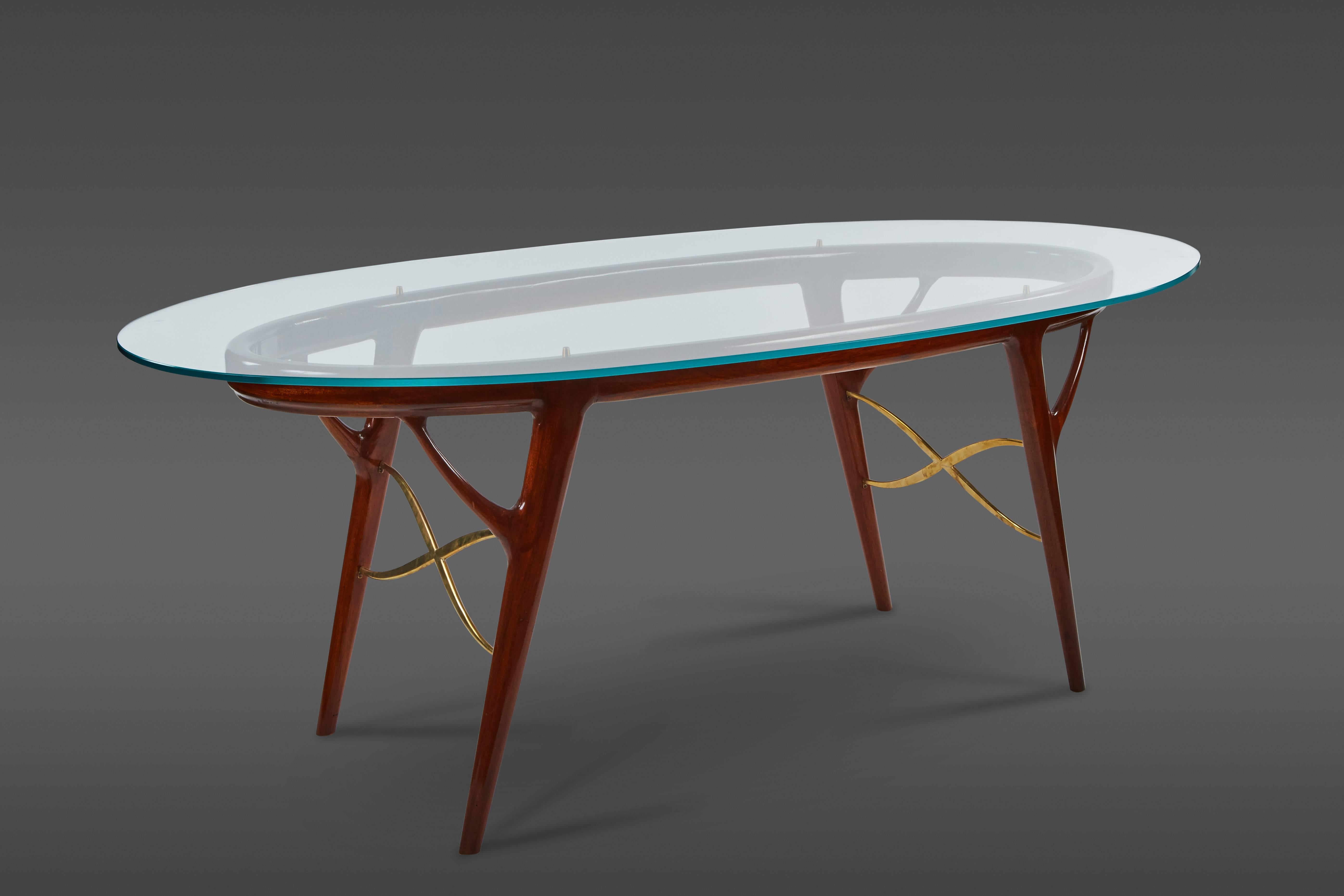 A striking oval table by Ico Parisi exhibiting a lacquered mahogany base, accentuated by graceful crossbars in brass. Its glass top rests on brass finials.