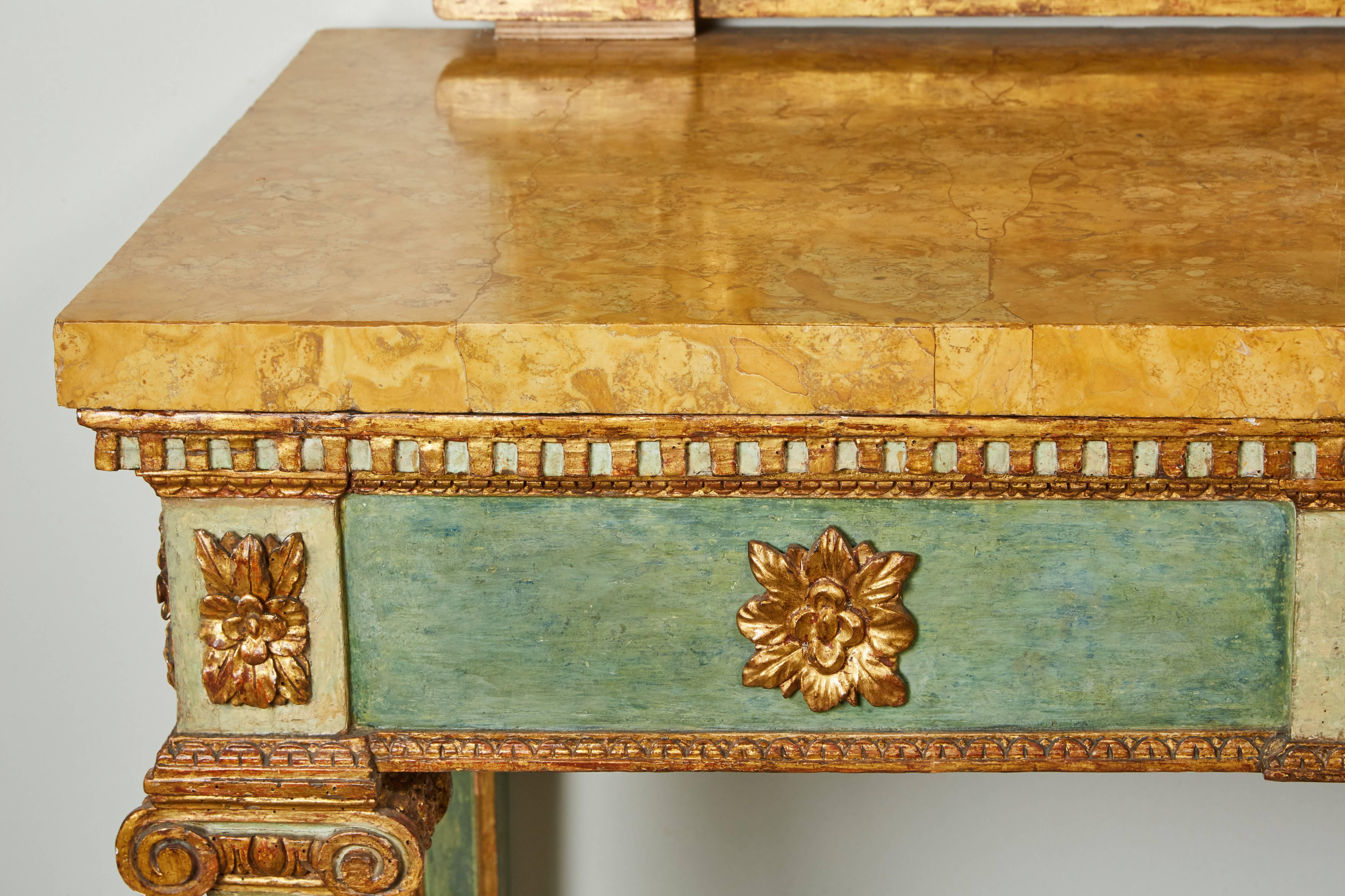 A striking late 18th century Italian parcel-gilt and blue-green painted mirror over console. 

The console table over square fluted legs 
capped between iconic capitals under a Giallo veneered marble top.
The mirror, exhibiting gilt foliate