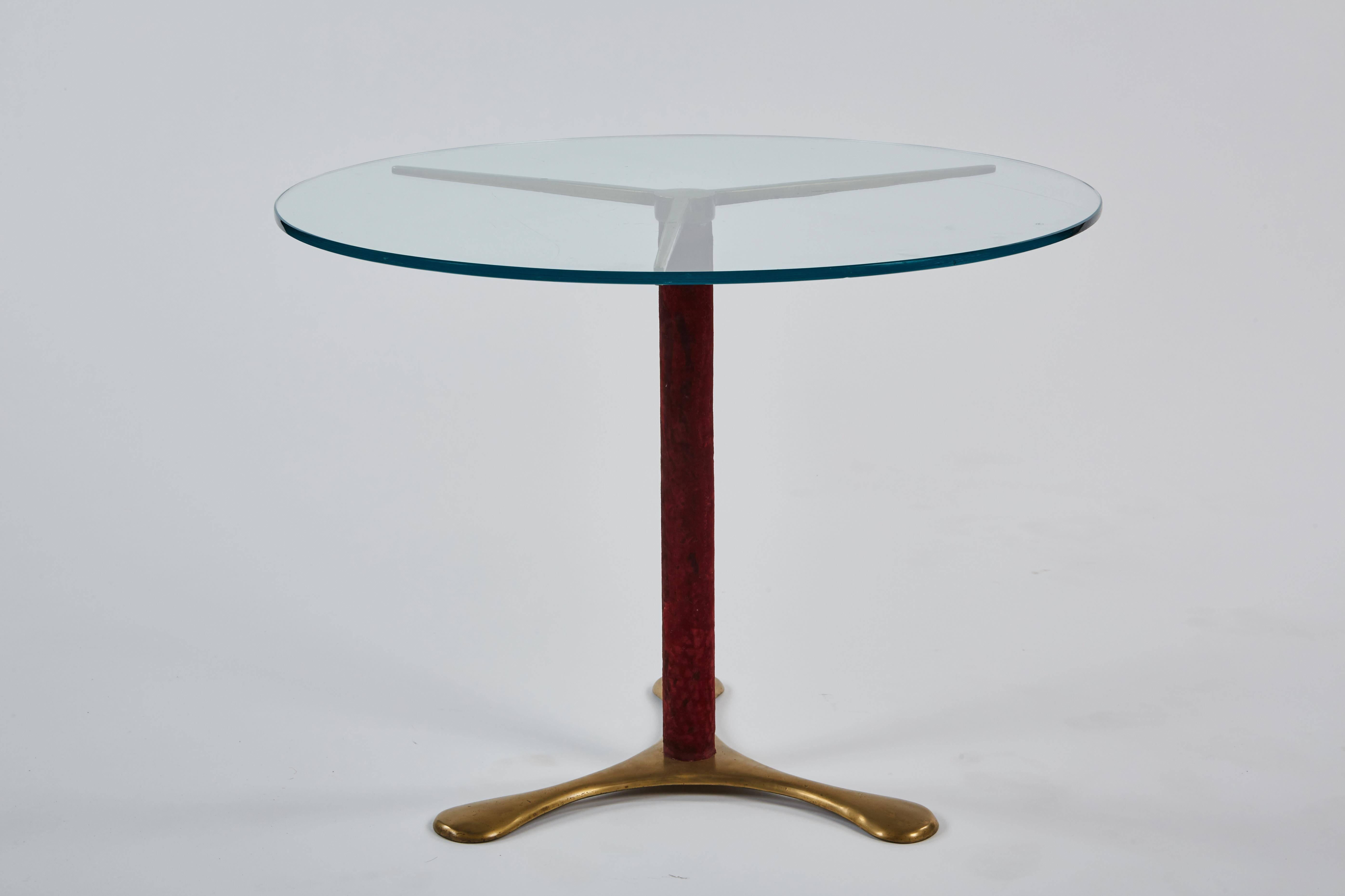 A delicate circular side table by Paolo Buffa, its glass top resting on a base of brass with a central upright in burgundy velvet.