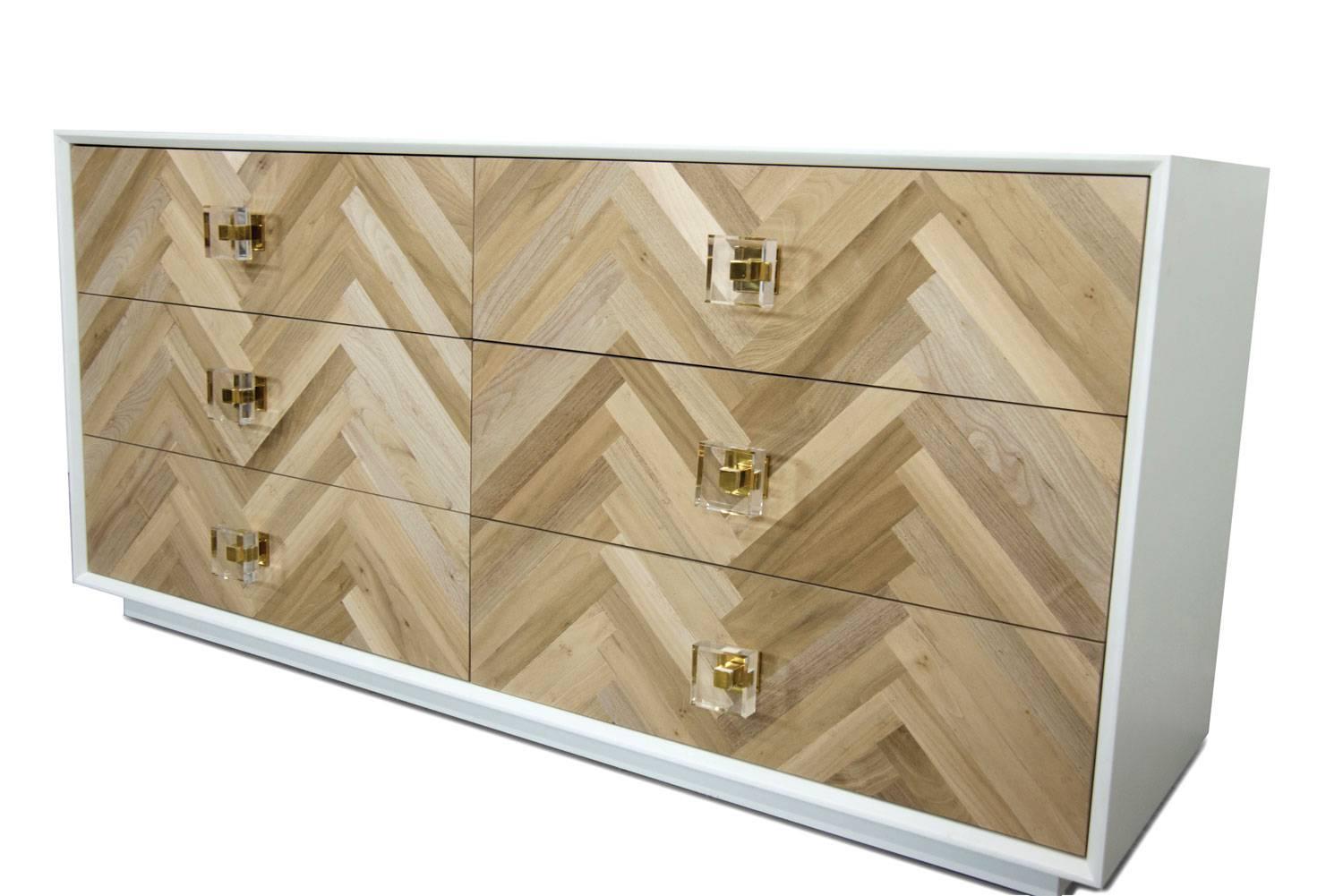 Our stylish new Amalfi dresser creates a solution to your storage needs. The door face is made of bleached walnut laid in chevron pattern. Together with matte white box and our beautiful brass and Lucite knobs creates the perfect mix of style and