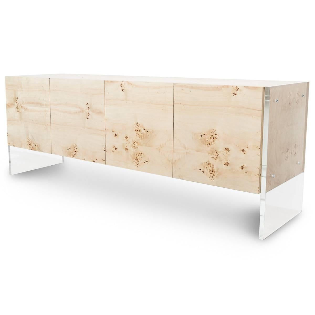 Mid-Century styling meets modern design with our new Credenza. This four door piece is wrapped in a beautiful Burl wood veneer and stands on large Lucite plinth legs that run the height of the credenza along the outside edges. The credenza stands 9