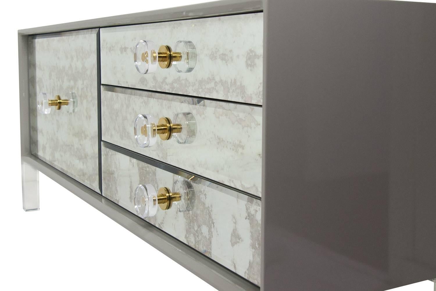 Juliette just went petite, the case is made in greystone lacquer finish, and has antiqued mirror door and drawer fronts. This antiqued look makes the piece a class of it's own. The use of the Lucite with brass round pulls creates the perfect mix of