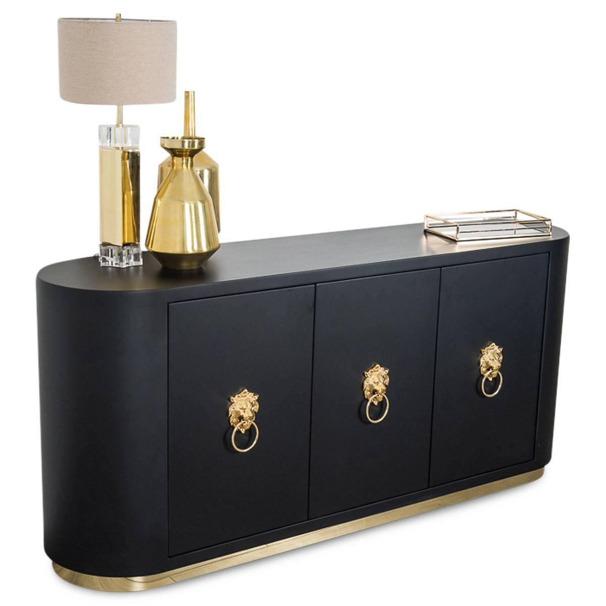 This stunning storage piece is a work of art. The new Art Deco inspired credenza is rounded at the ends. It has three doors adorned with brass, Lion Head knockers. The credenza is a matte black with a 2 inch toe kick made of brass. It also has two